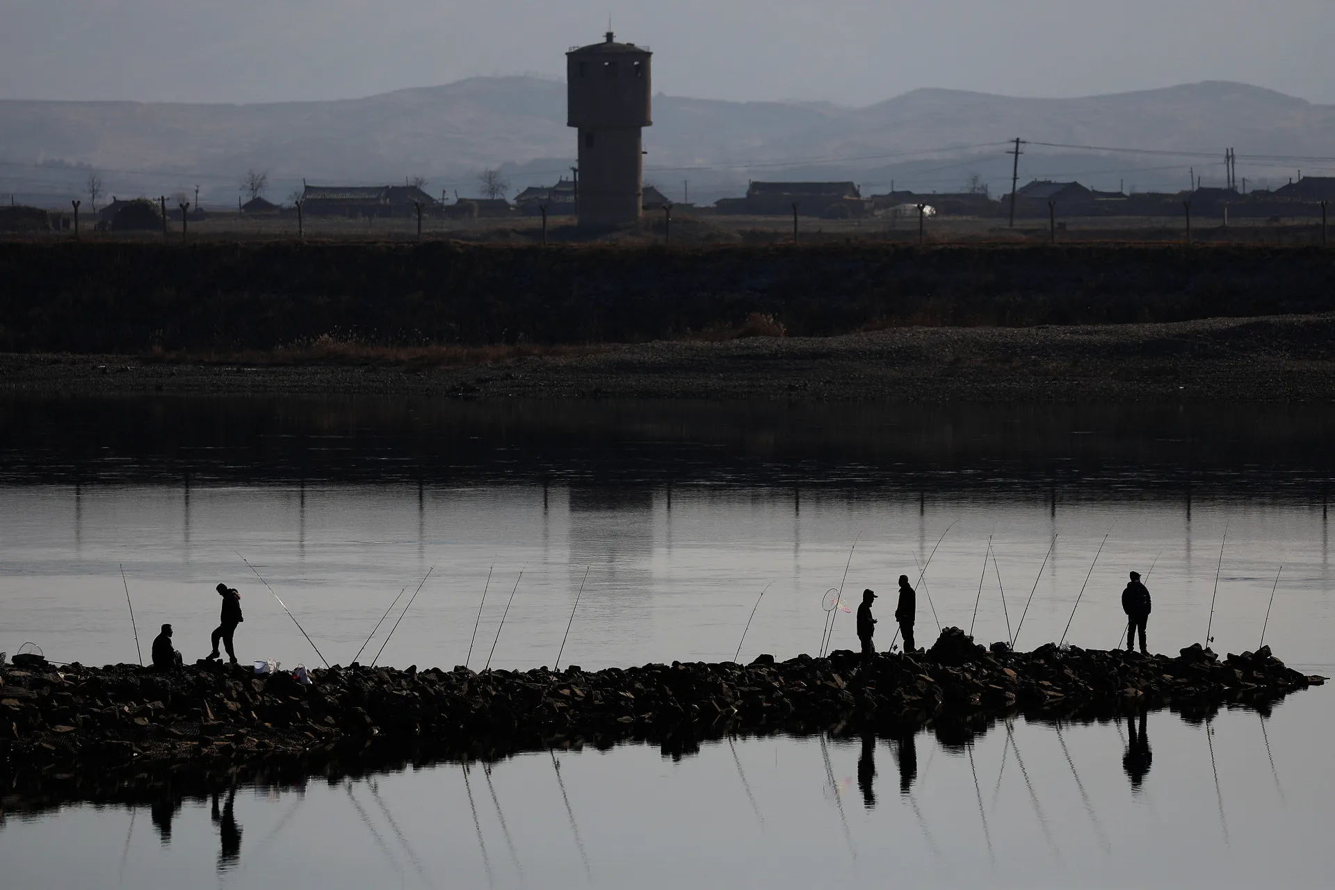 Pescadores chineses no rio Yalu com uma torre de vigilância norte-coreana ao fundo.