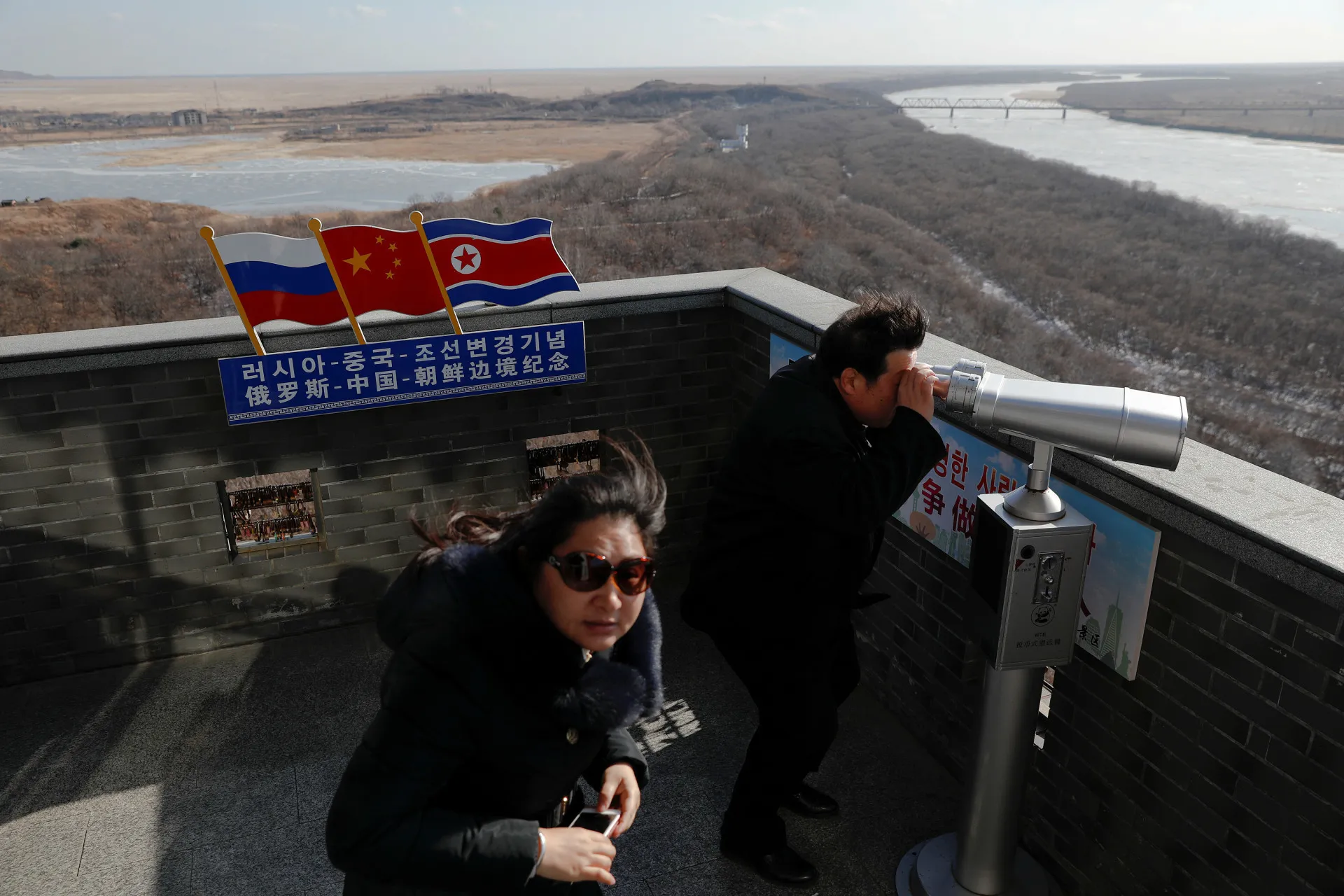 Turista em uma torre de vigilância chinesa usando binóculos para ver a Coreia do Norte.