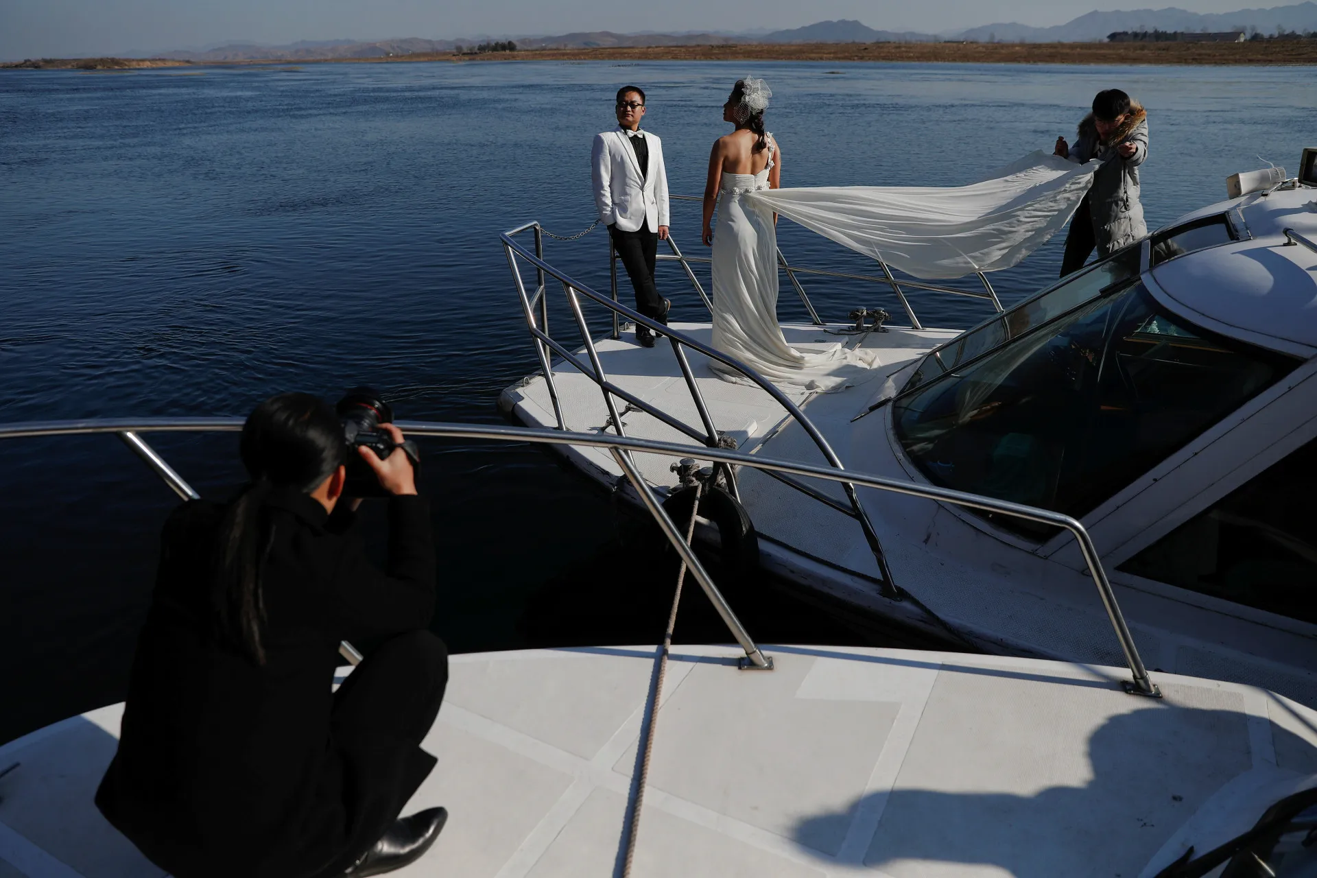 Casal de recém-casados posando para fotos de casamento em um barco no rio Yalu.