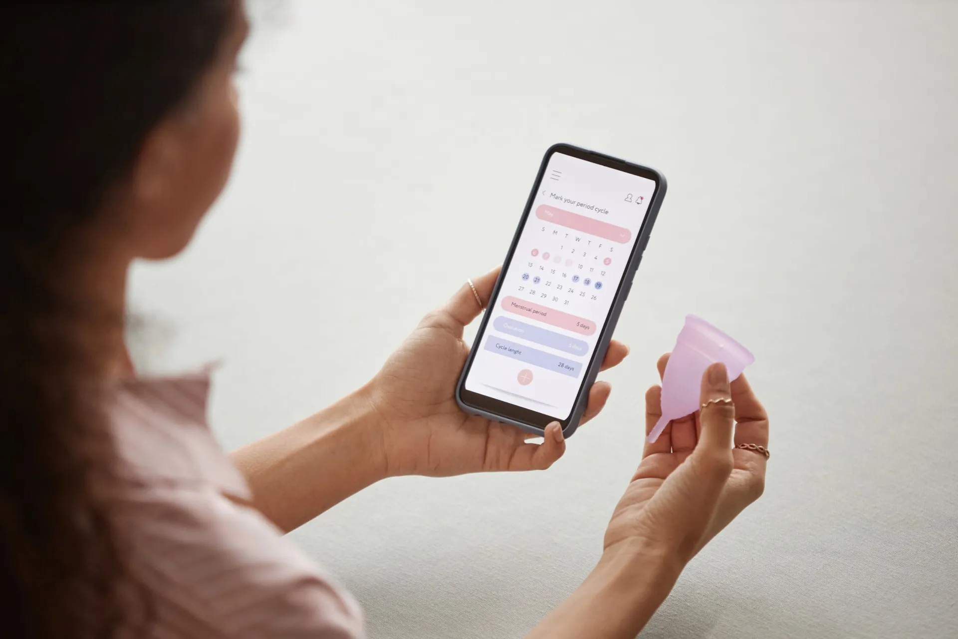 Calendário menstrual sendo exibido na tela de um smartphone, com marcações de ciclo.
