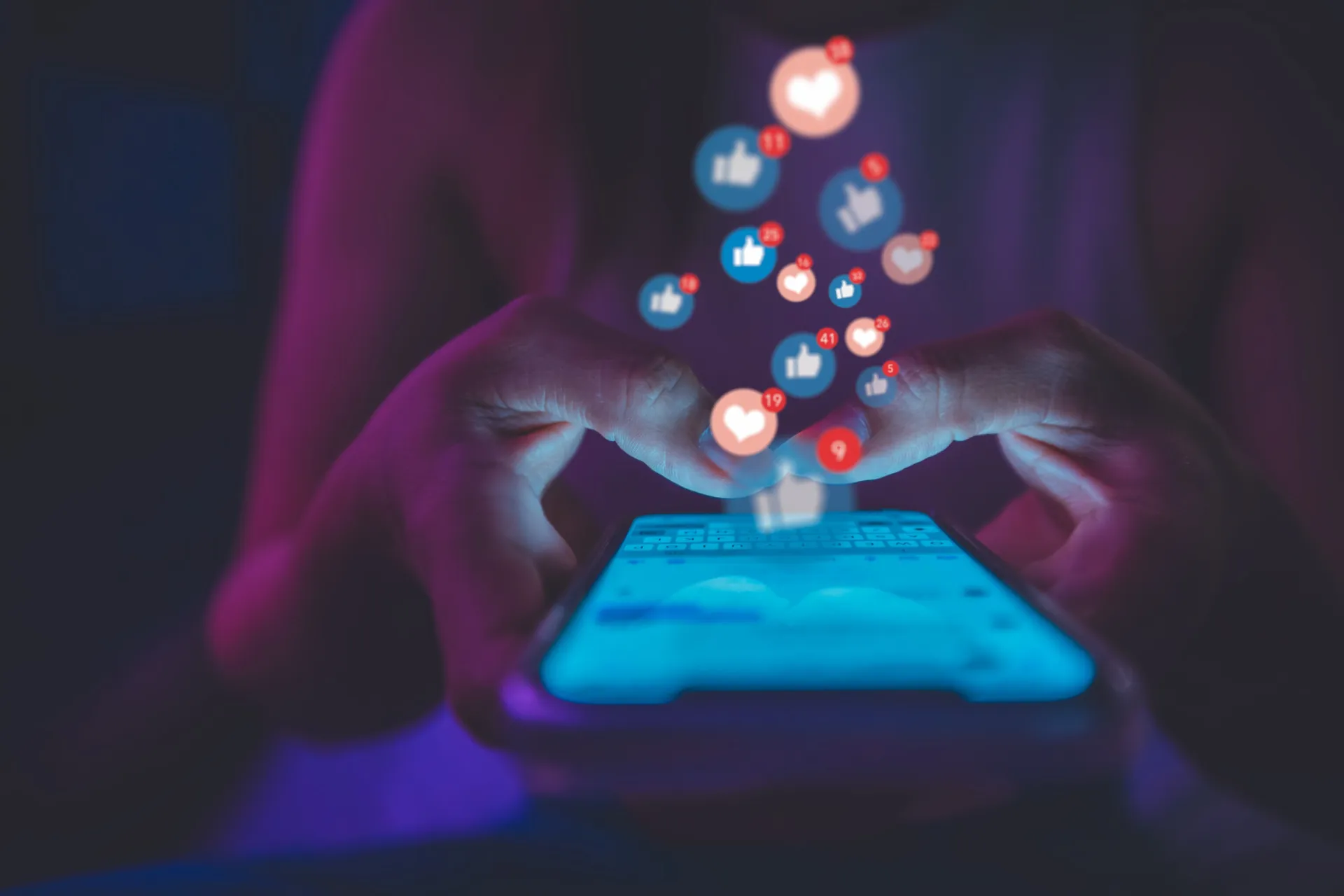 Ícones de curtida, comentário e compartilhamento sendo manipulados por uma pessoa no celular.