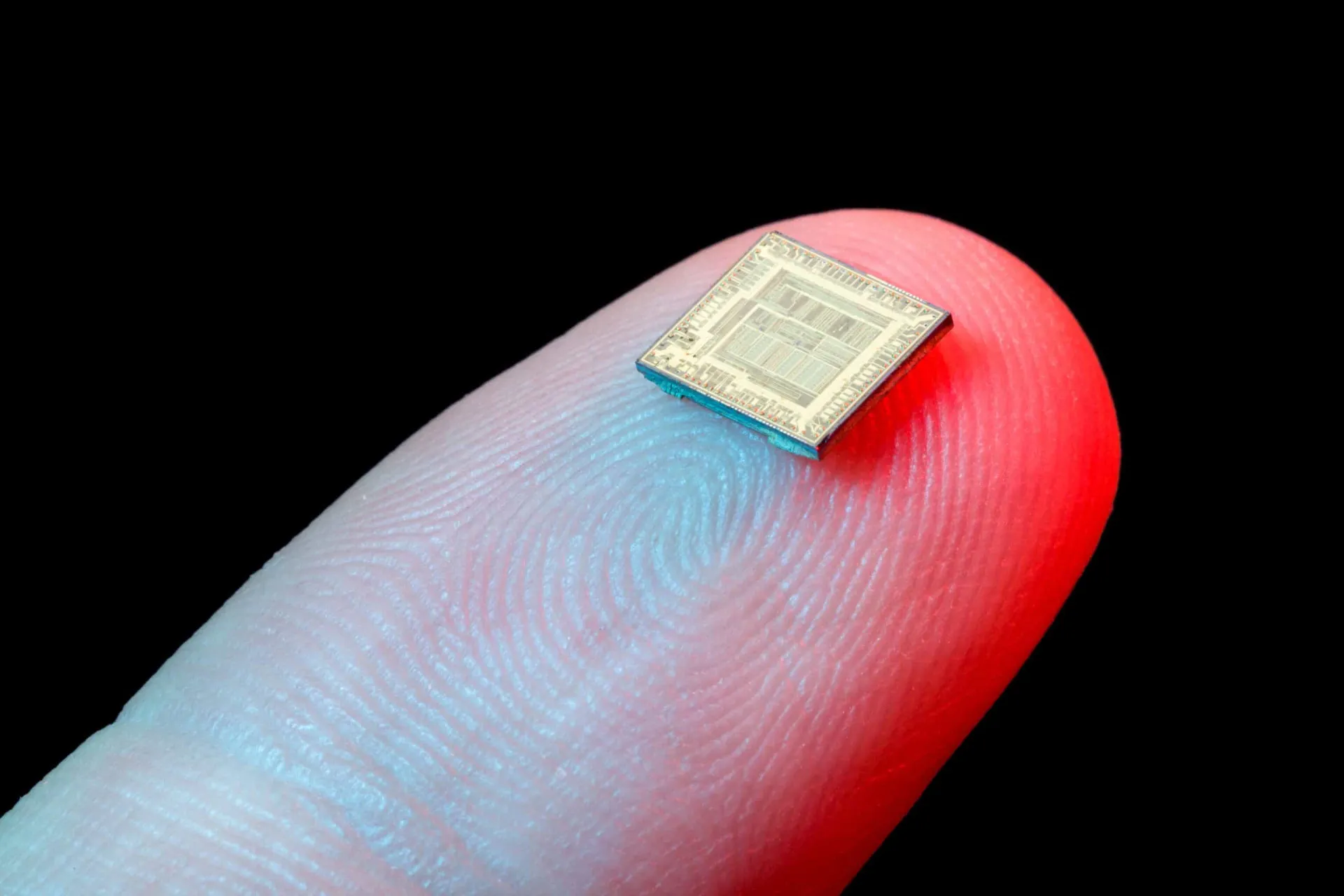 Mão segurando um pequeno objeto metálico que se parece com um chip ou implante.