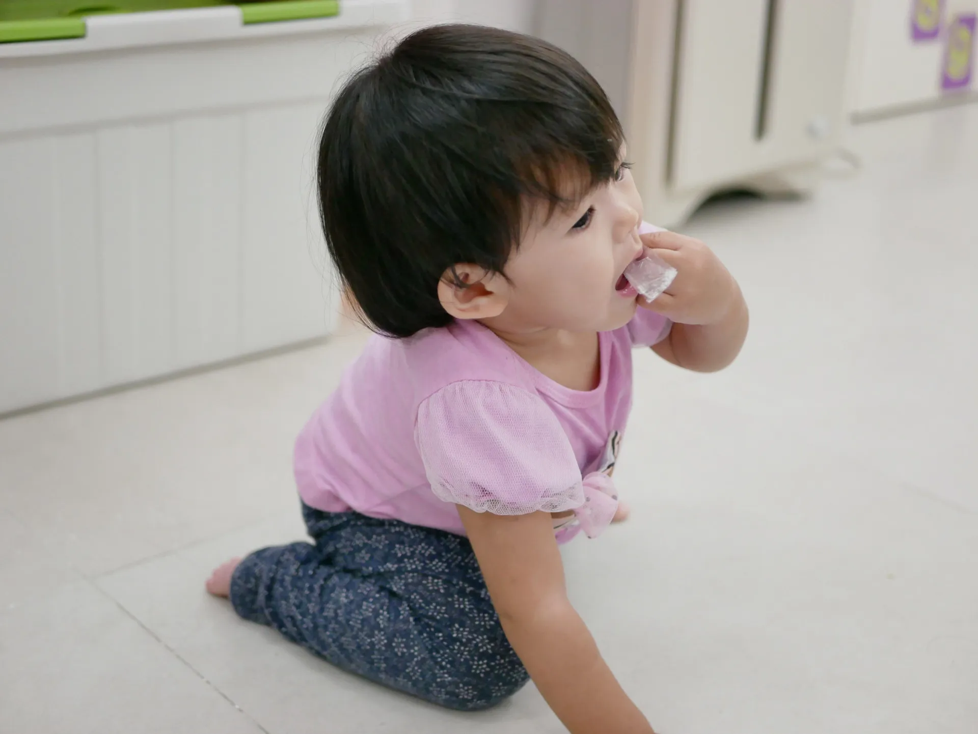 Bebê sentado no chão colocando um objeto pequeno na boca.