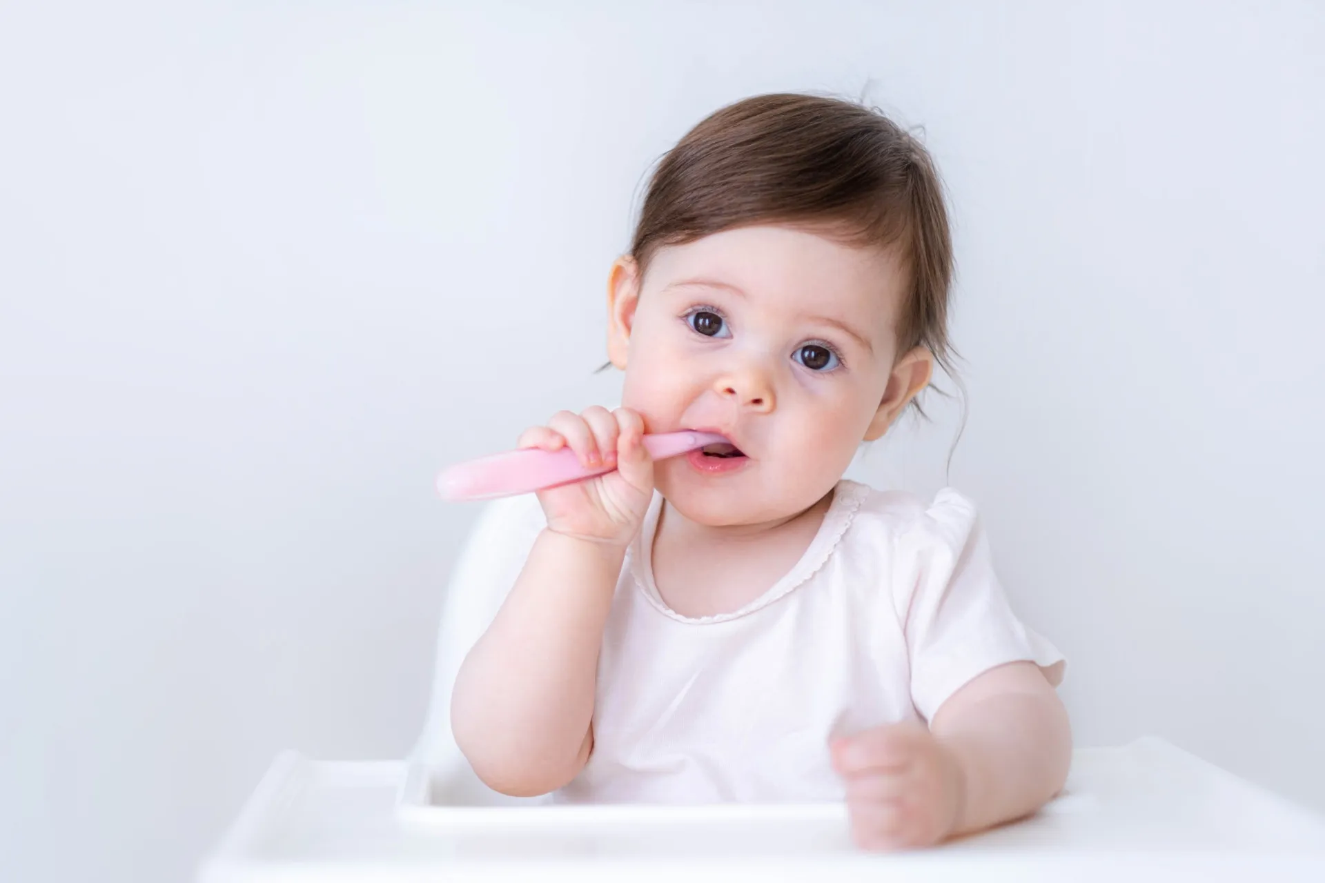 Criança pequena brincando no chão perto de pequenos objetos coloridos, representando um risco.