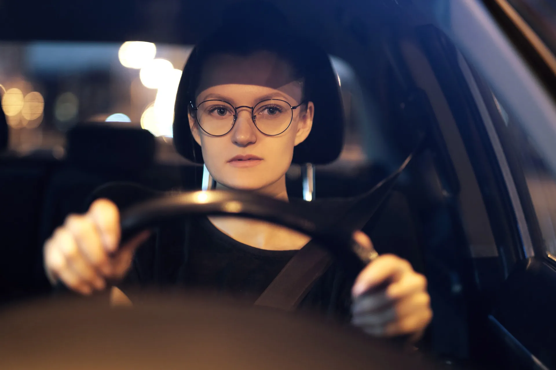Visão de dentro de um carro, com as mãos no volante e a estrada à frente.