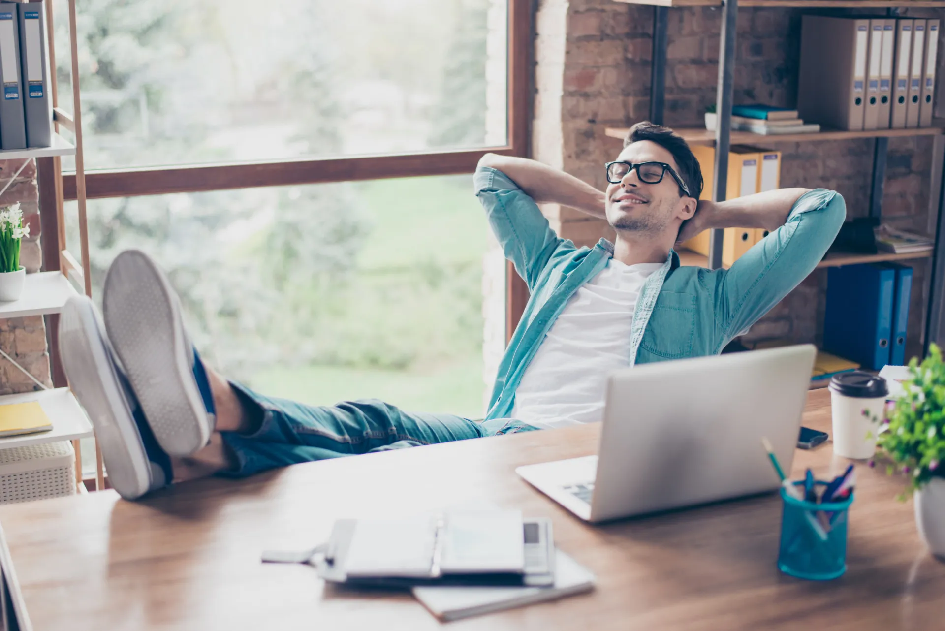 Pessoa se espreguiçando em sua mesa de trabalho, fazendo uma pausa da tela do computador.