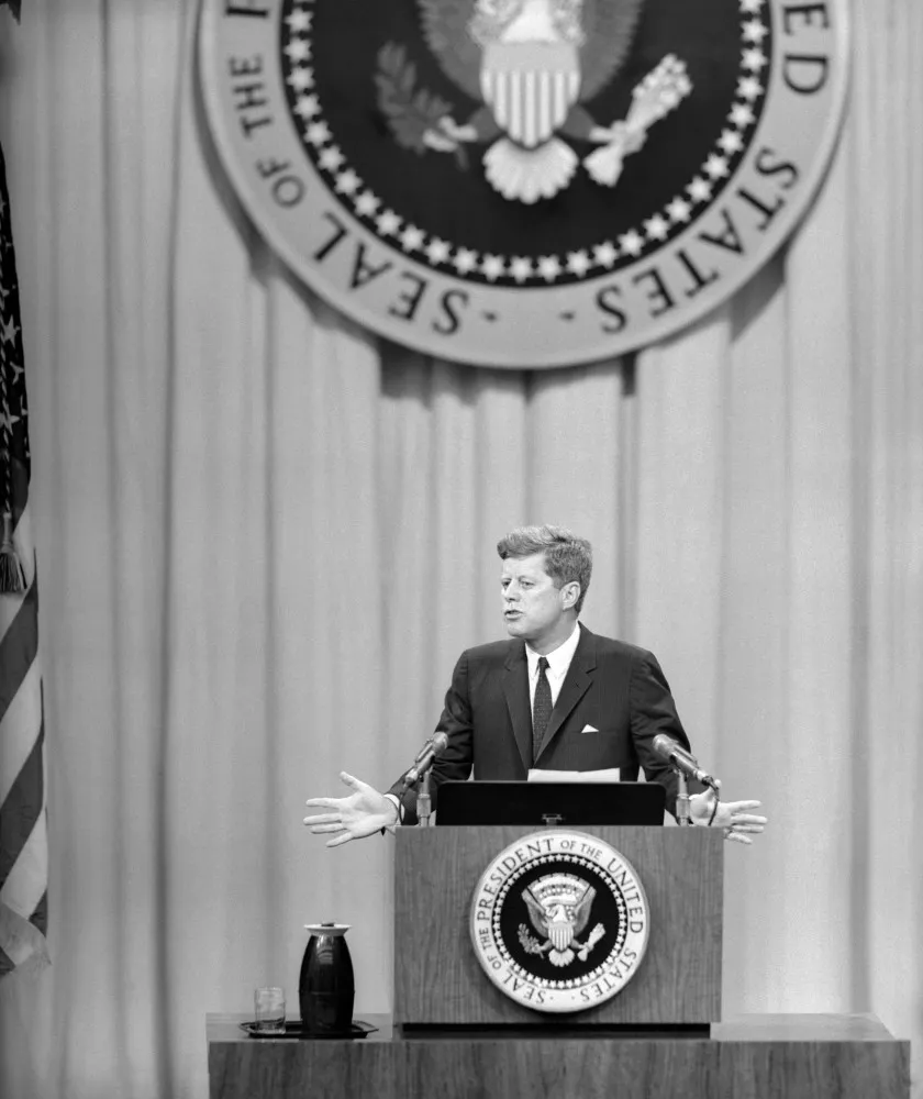 John F. Kennedy apontando para um mapa do Sudeste Asiático, explicando a Teoria do Dominó.