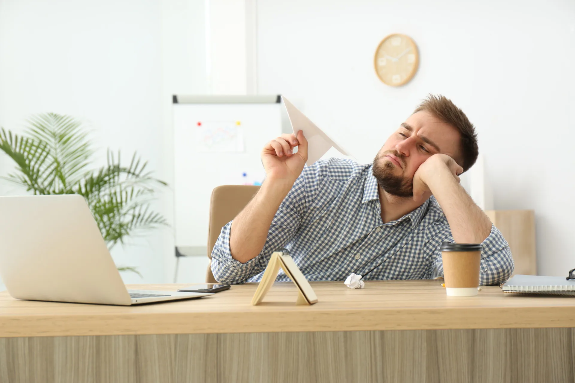 Pessoa bocejando de tédio em sua mesa de trabalho, cercada por papéis.