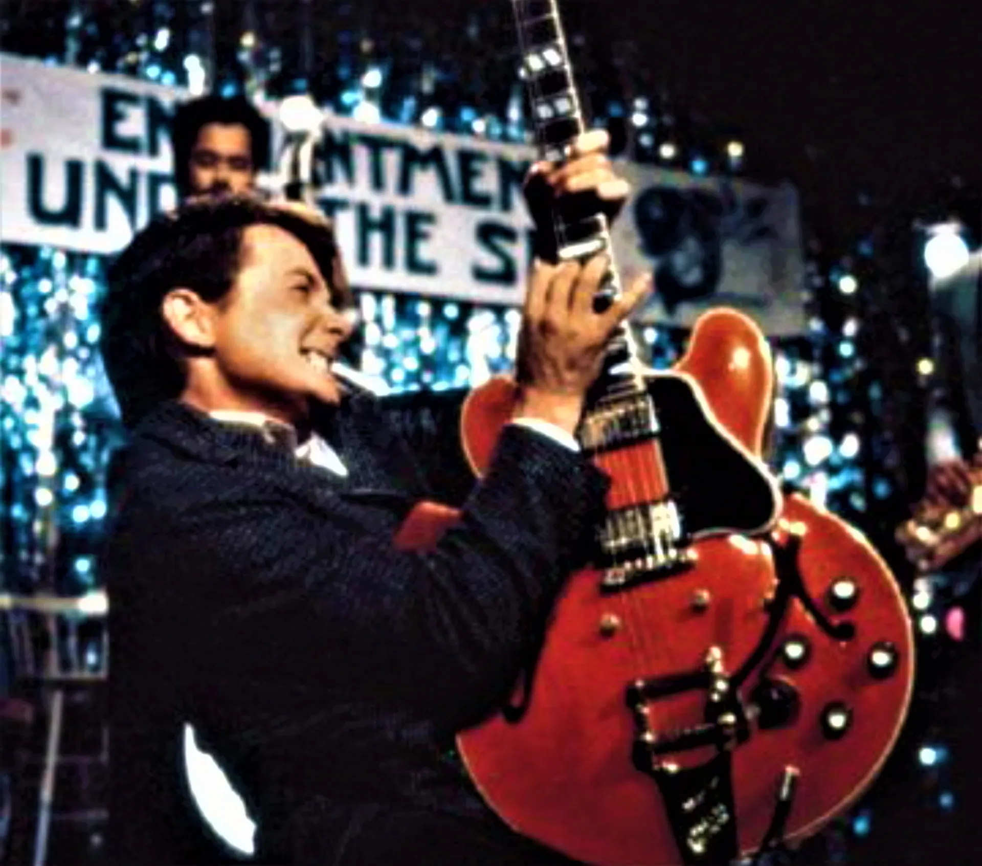 Marty McFly tocando a música 'Johnny B Goode' com uma guitarra vermelha no palco.