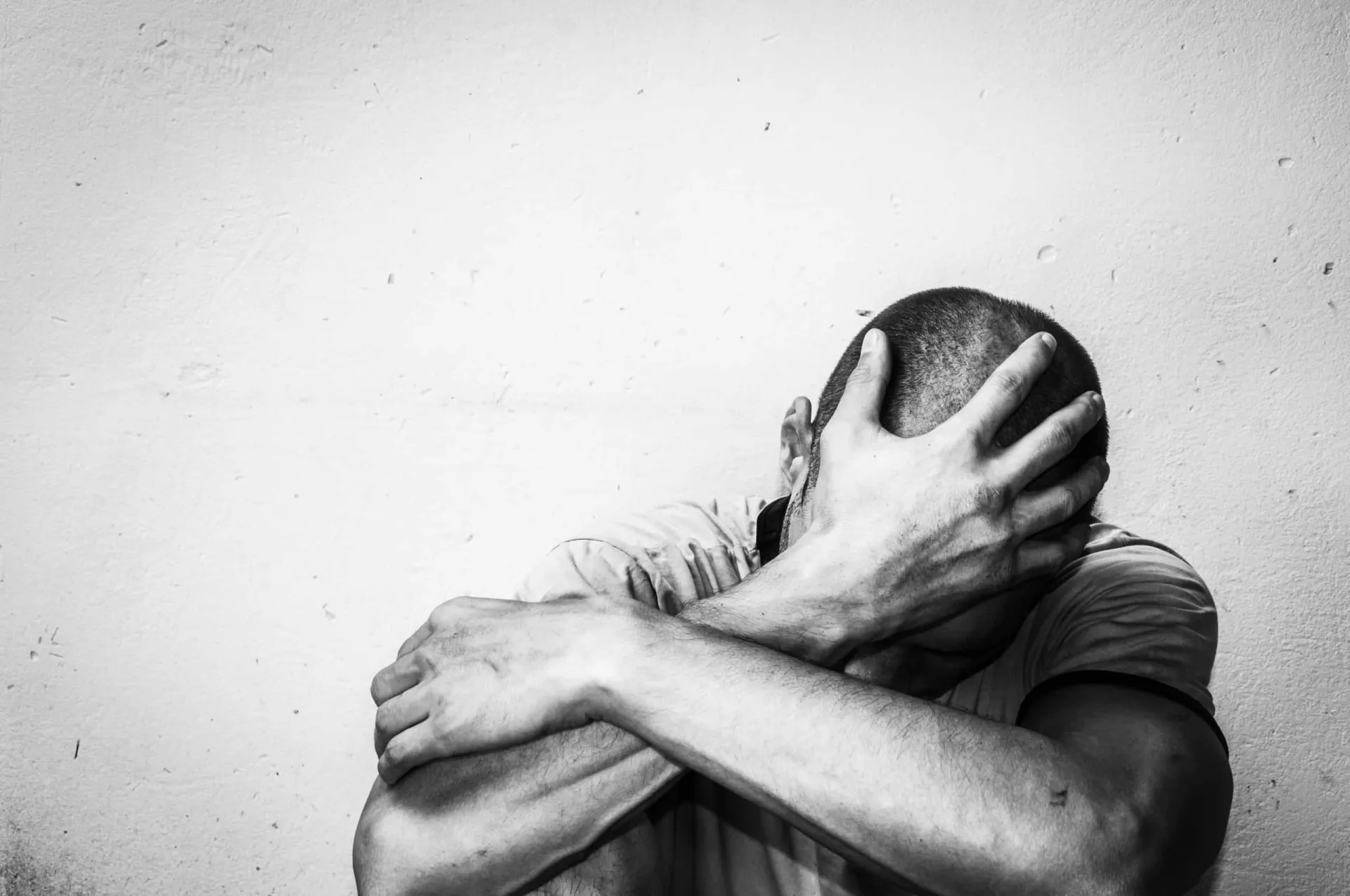 Homem olhando pela fresta de uma persiana, com expressão de paranoia.