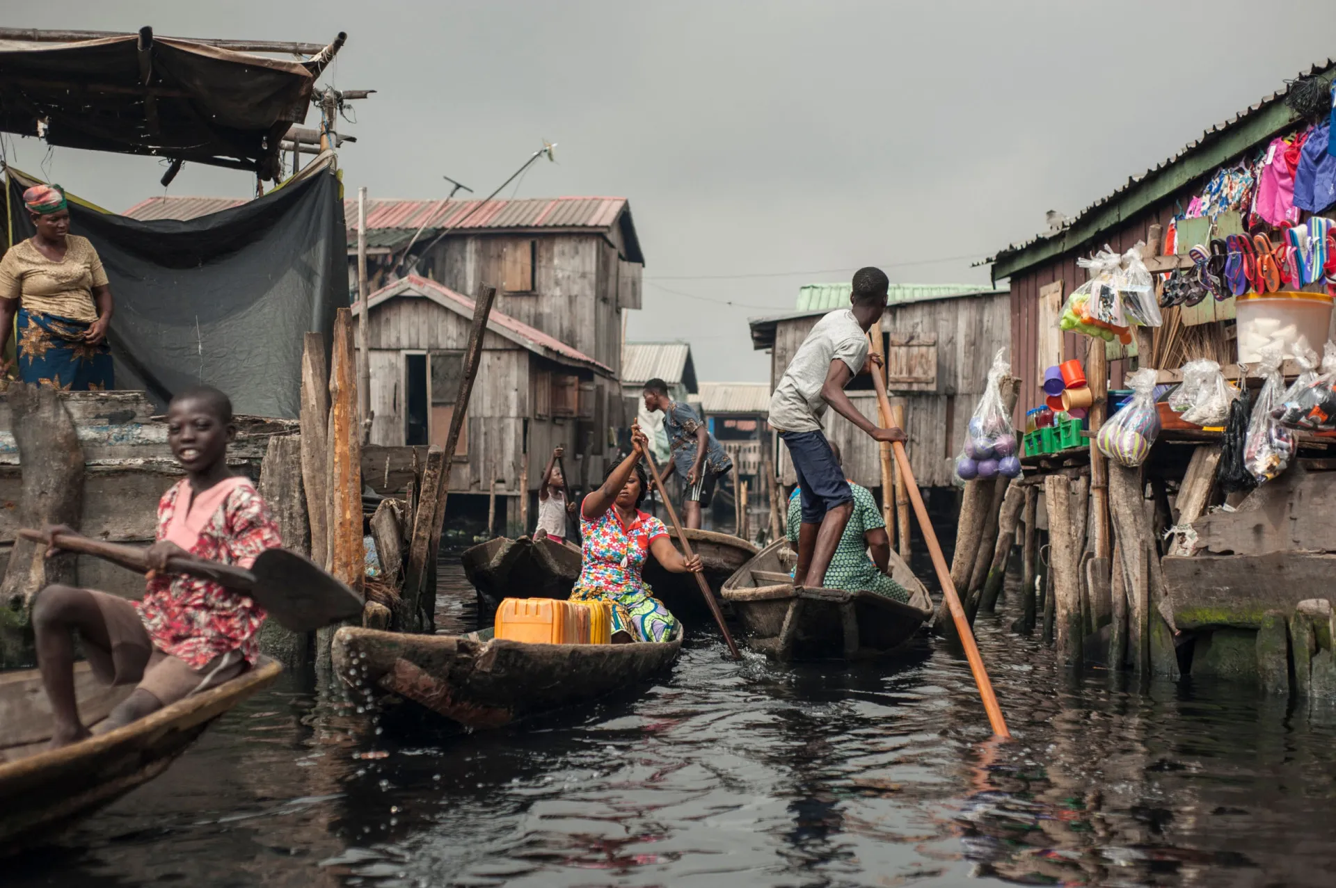 Crianças em uma canoa navegando pelos canais de Makoko, com as casas de palafitas ao redor.