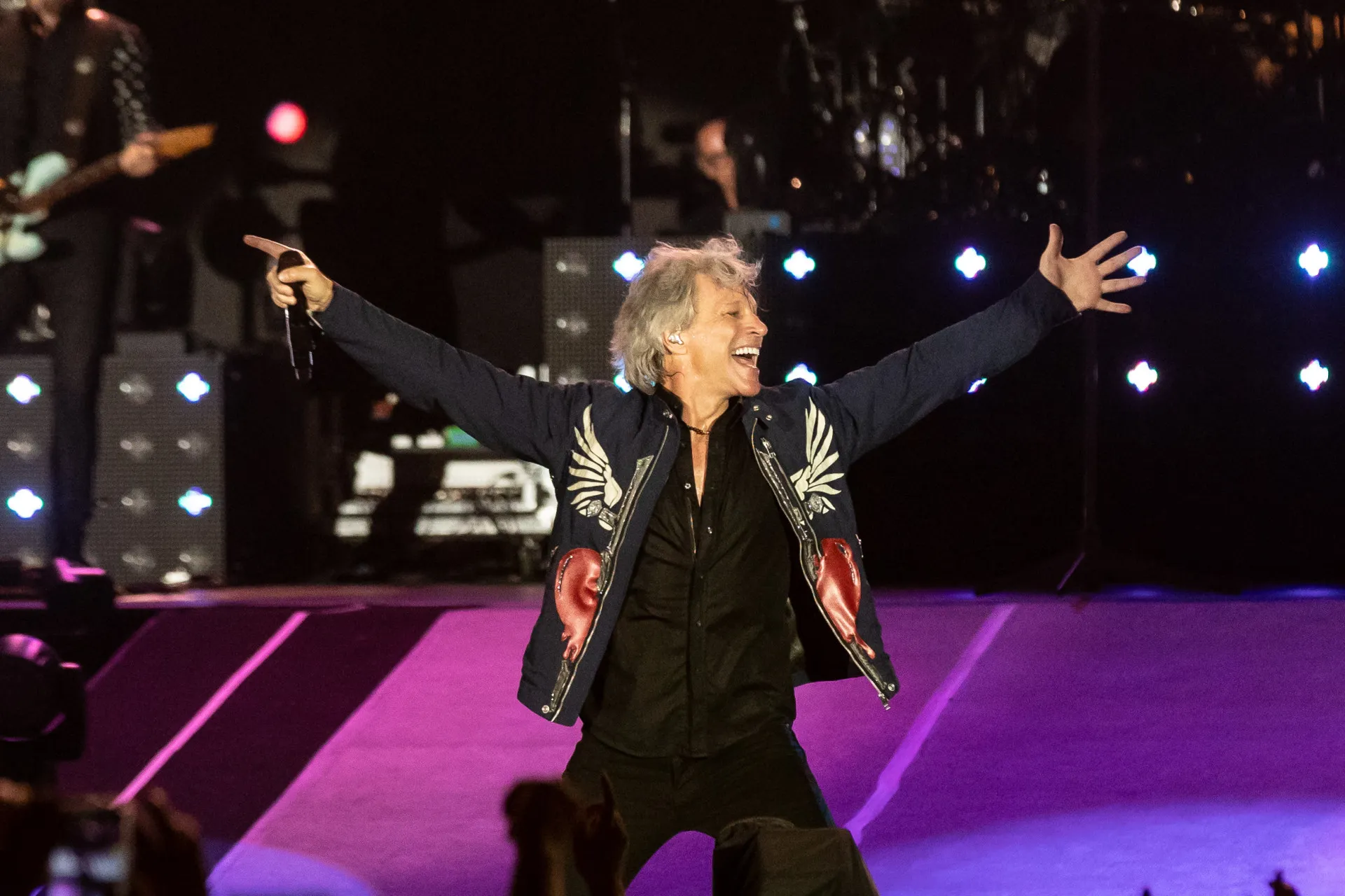 Jon Bon Jovi com seu cabelo icônico dos anos 80, cantando com energia no palco.