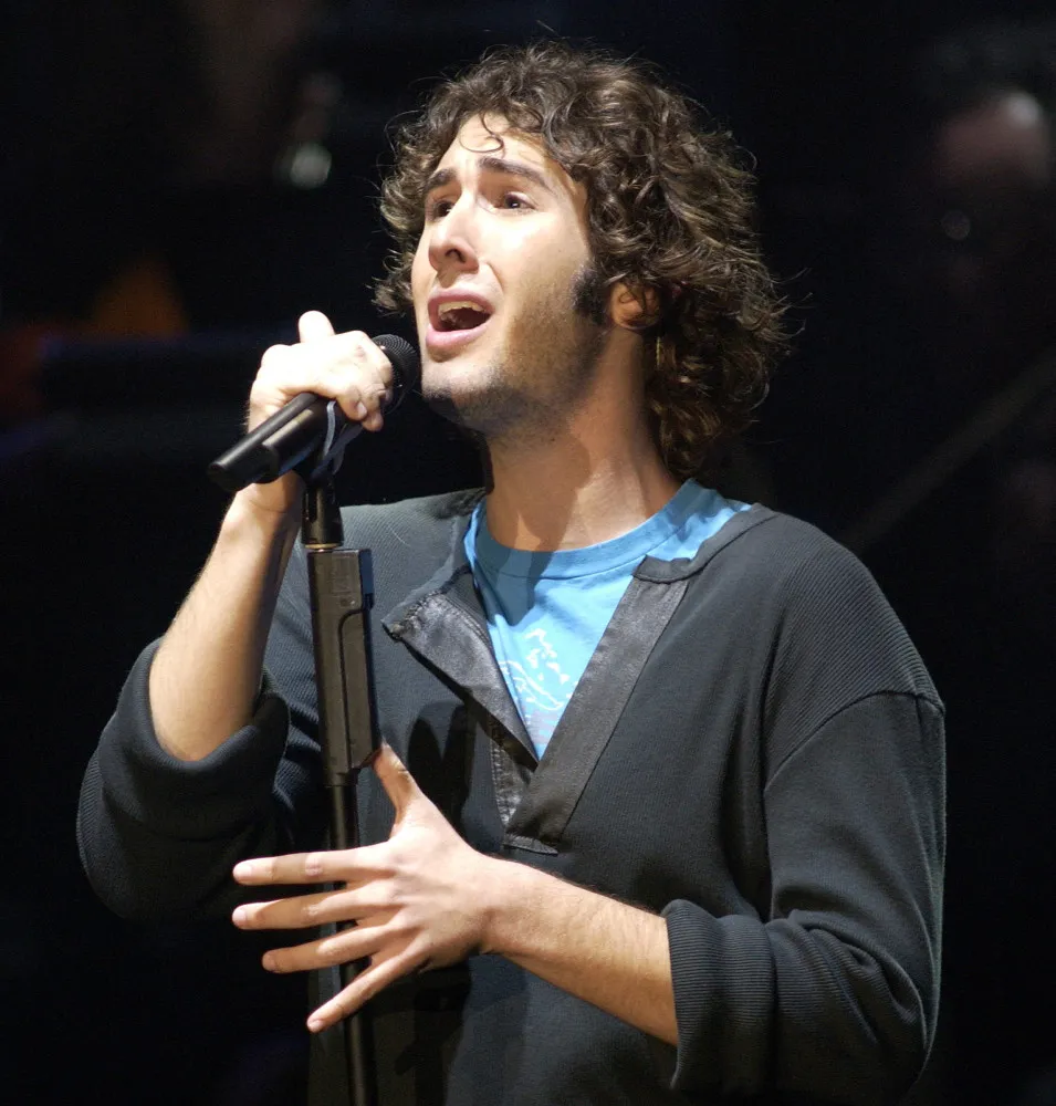 Josh Groban em um terno elegante, cantando com seriedade em um evento.