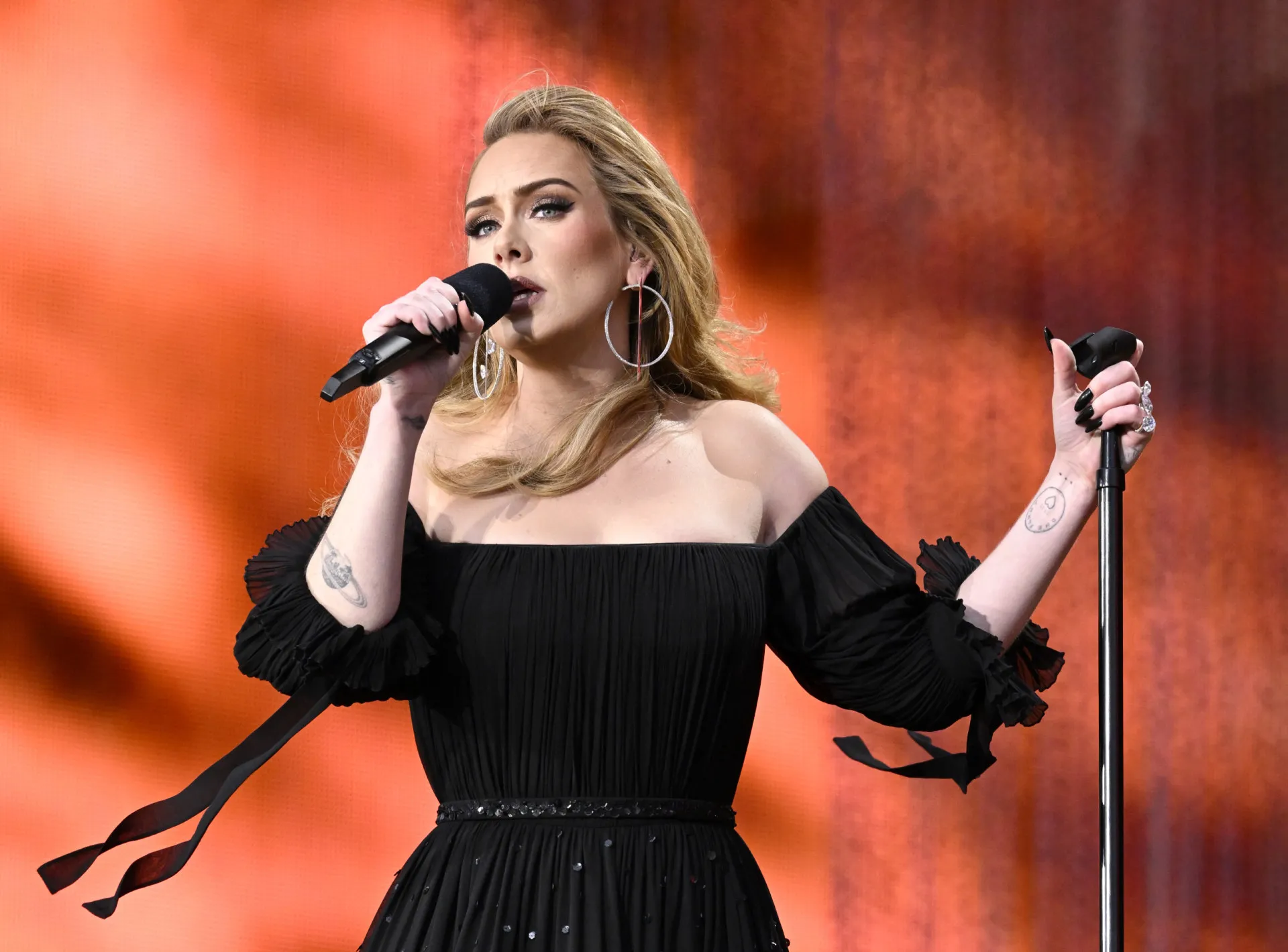 Adele cantando com os olhos fechados, transmitindo uma emoção profunda.