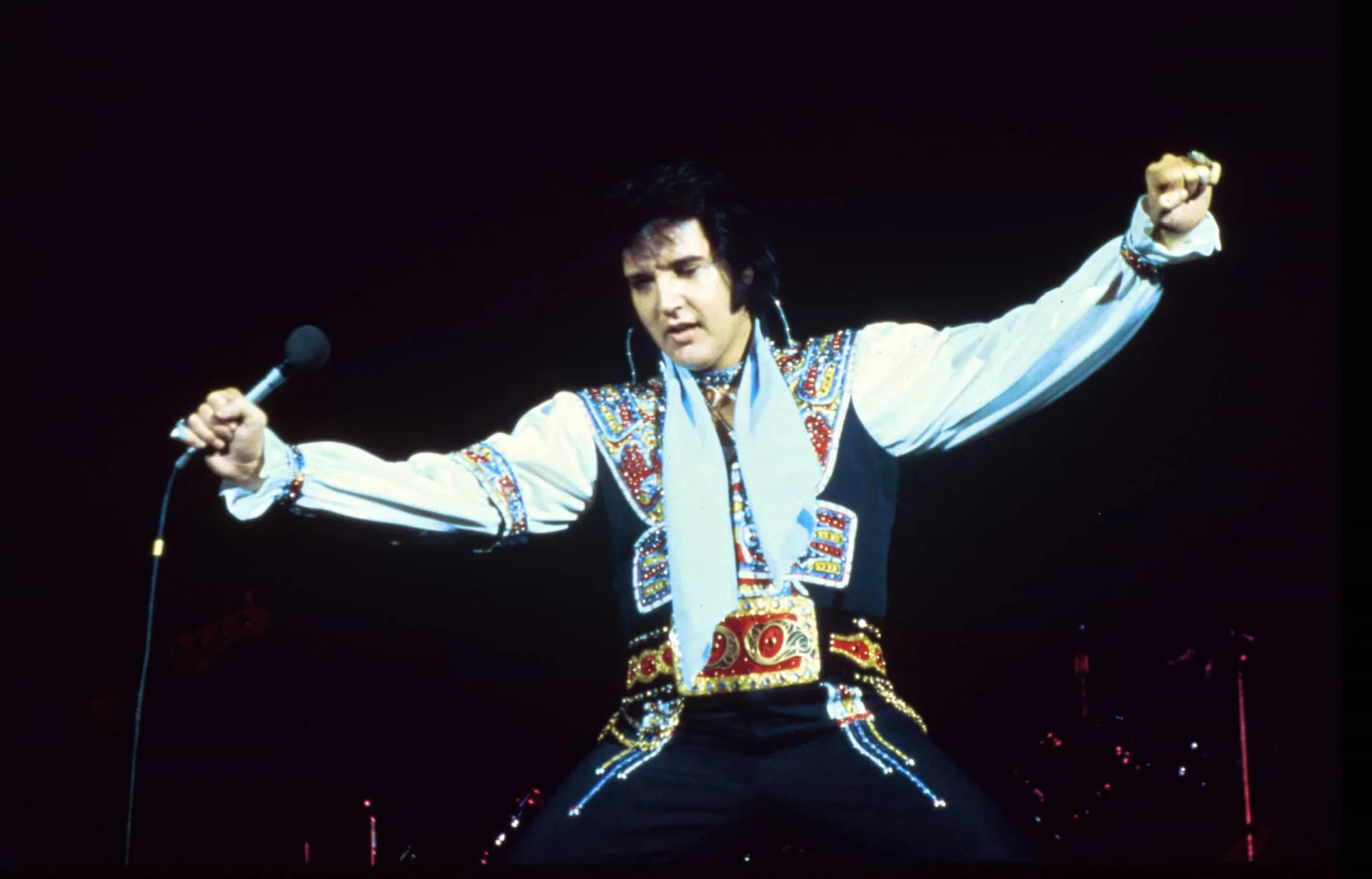 Elvis Presley, o Rei do Rock, em uma pose icônica com seu famoso topete e sorriso de lado.