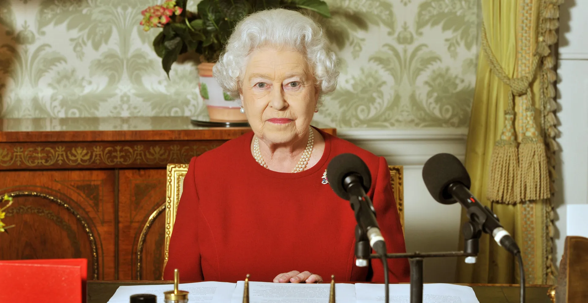 Rainha Elizabeth II sorrindo, usando um chapéu e traje formal em um evento público.