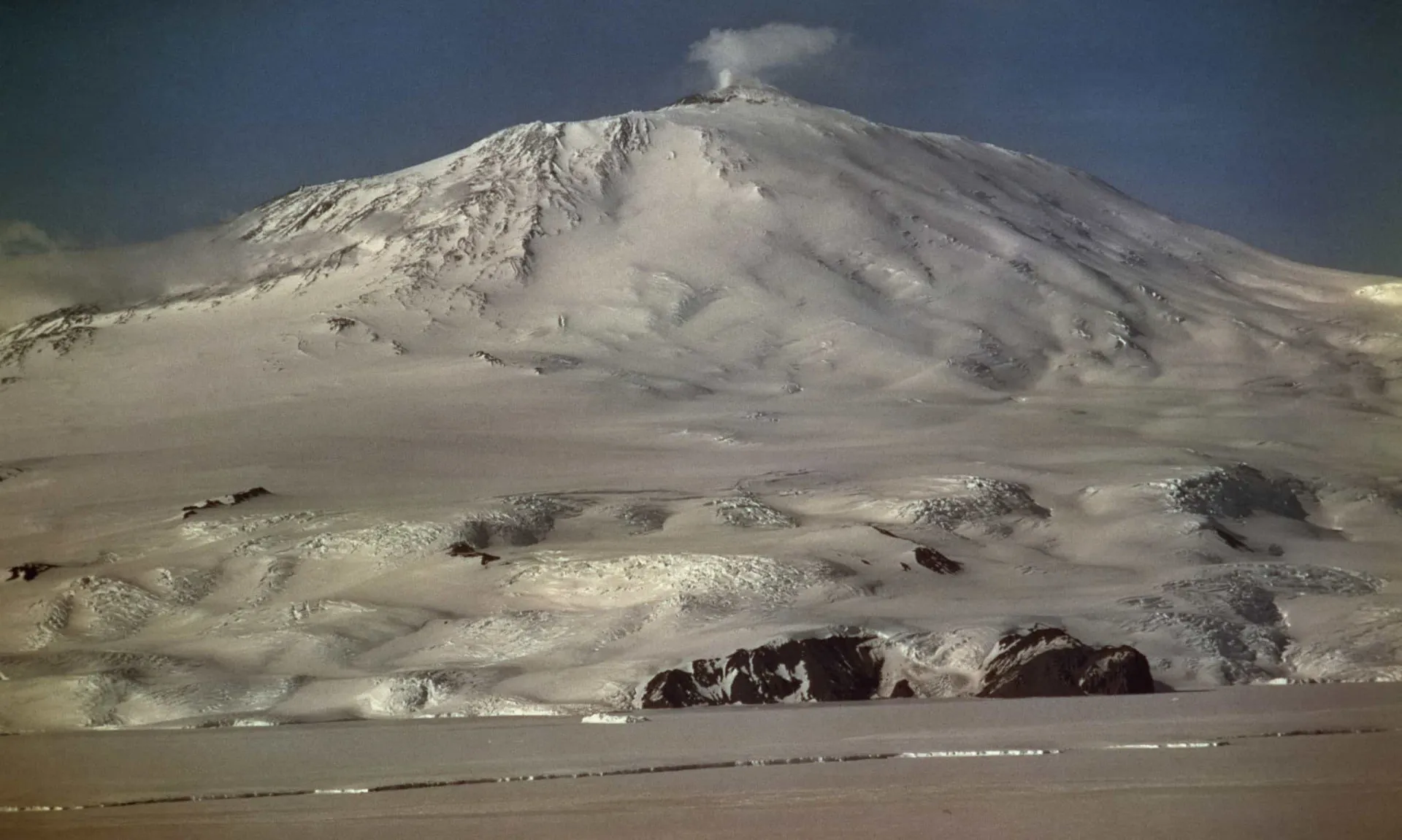 O Monte Erebus, um vulcão coberto de neve na Antártica, com fumaça saindo de sua cratera.