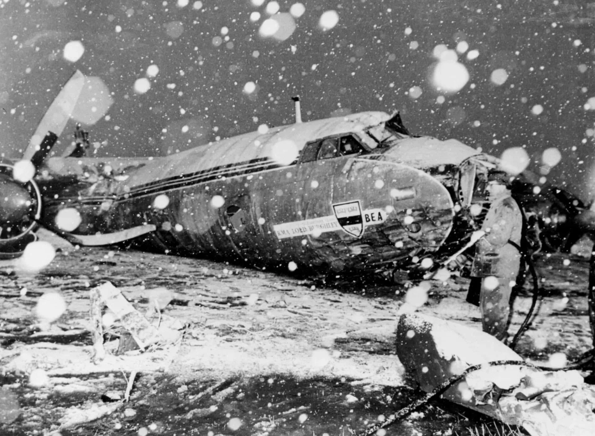 Destroços de um avião em uma paisagem nevada, com uma casa danificada ao fundo.