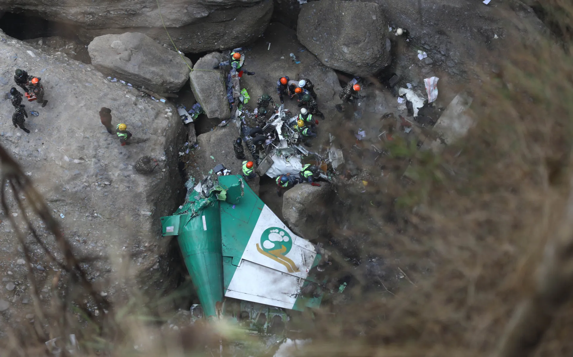 Equipes de resgate procurando por vítimas em meio aos destroços de um avião em um desfiladeiro.