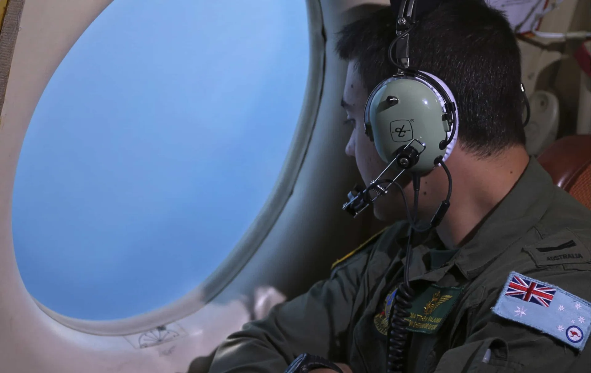Um membro da tripulação de um avião de busca olhando pela janela para o vasto oceano.