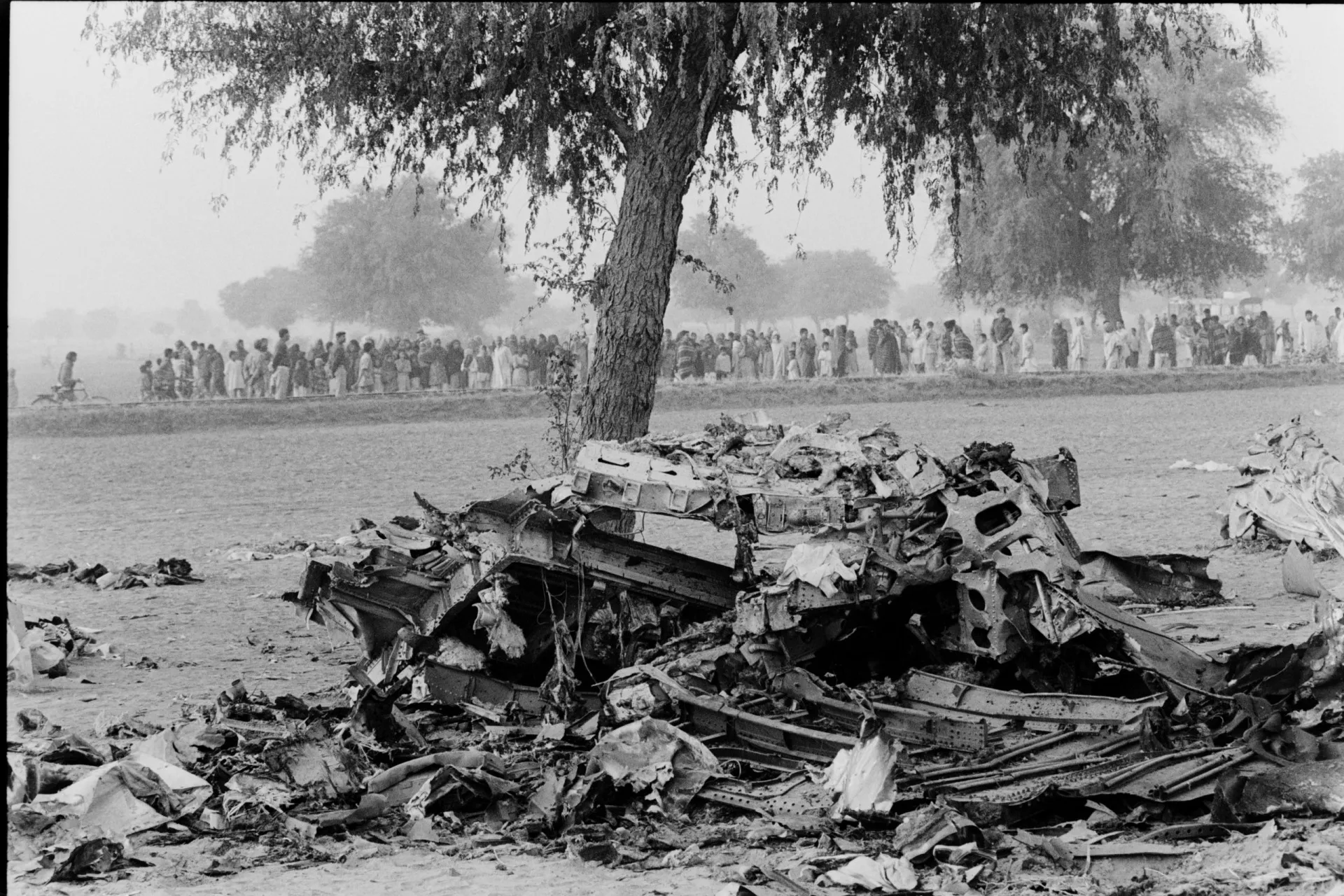 Destroços retorcidos de dois grandes aviões em um campo, cercados por uma multidão.