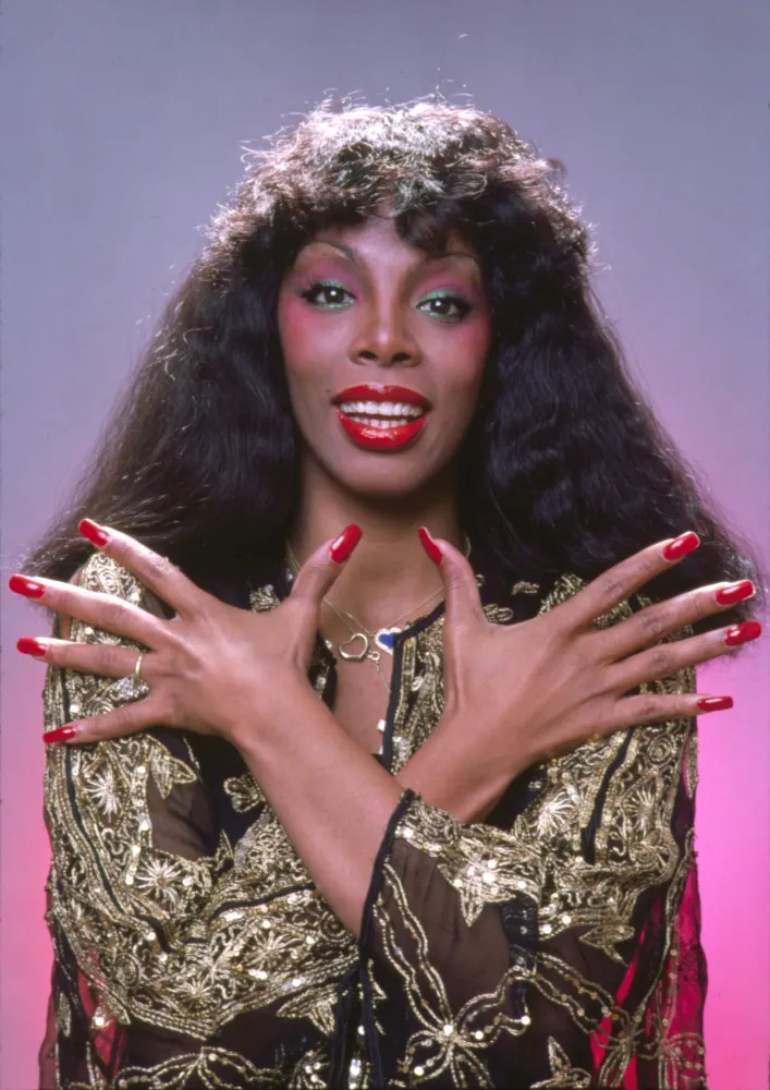 Donna Summer em uma pose poderosa no palco, simbolizando a era da Disco.