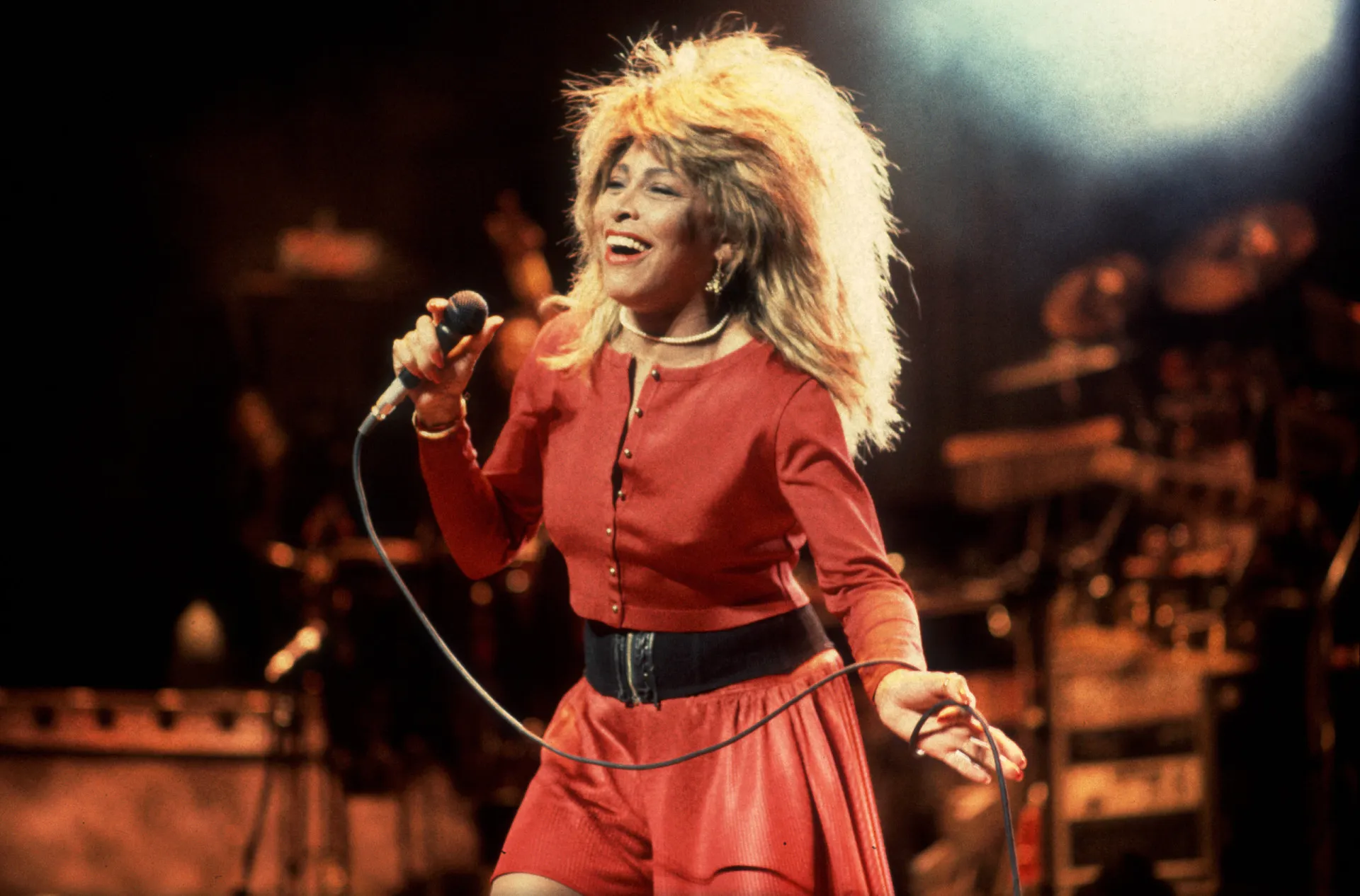 Tina Turner no palco com sua energia inconfundível e cabelo icônico.
