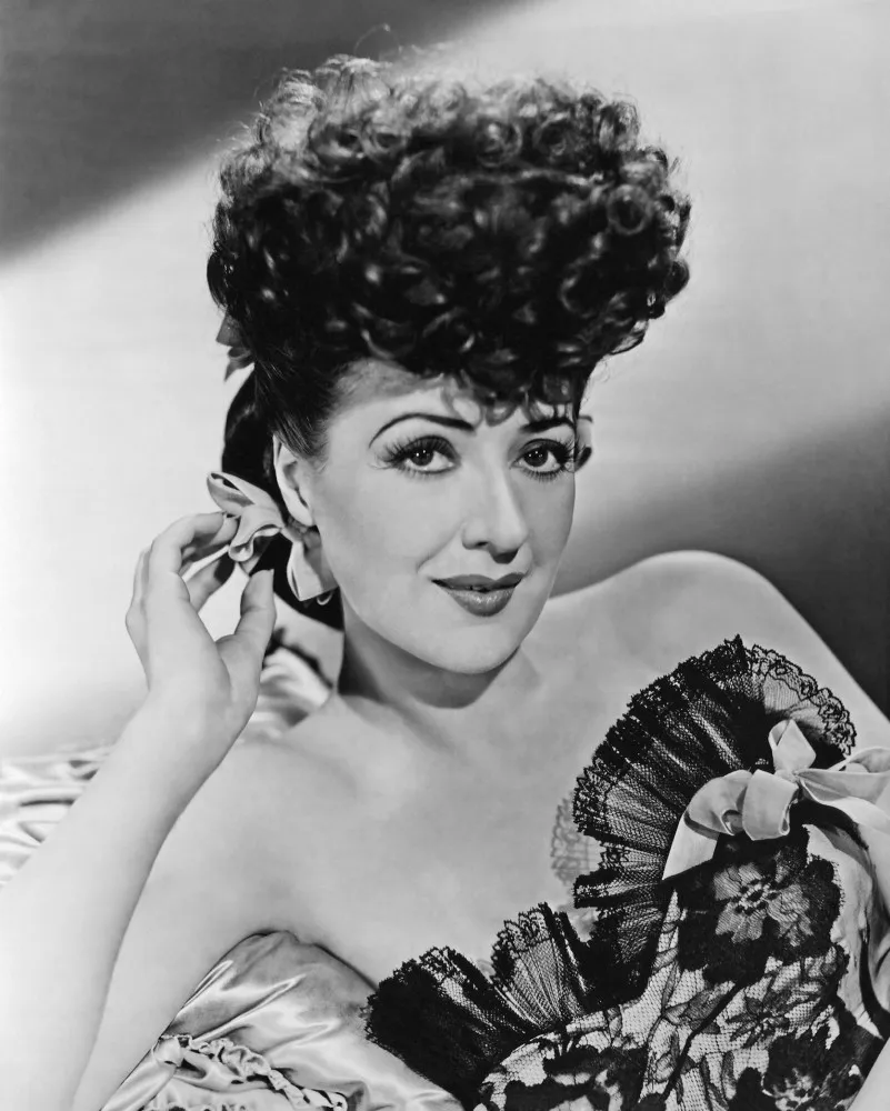 Gypsy Rose Lee em uma pose clássica, com um sorriso confiante e um olhar sedutor.