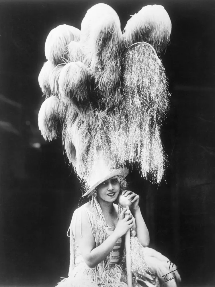 Mistinguett em um retrato de época, com um chapéu de plumas e um olhar marcante.