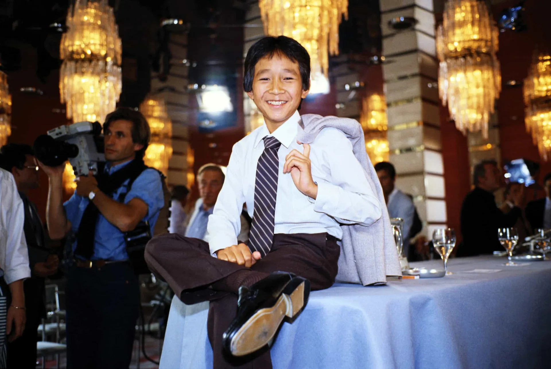 O ator Ke Huy Quan em sua juventude, com um sorriso no rosto, em um evento de tapete vermelho.