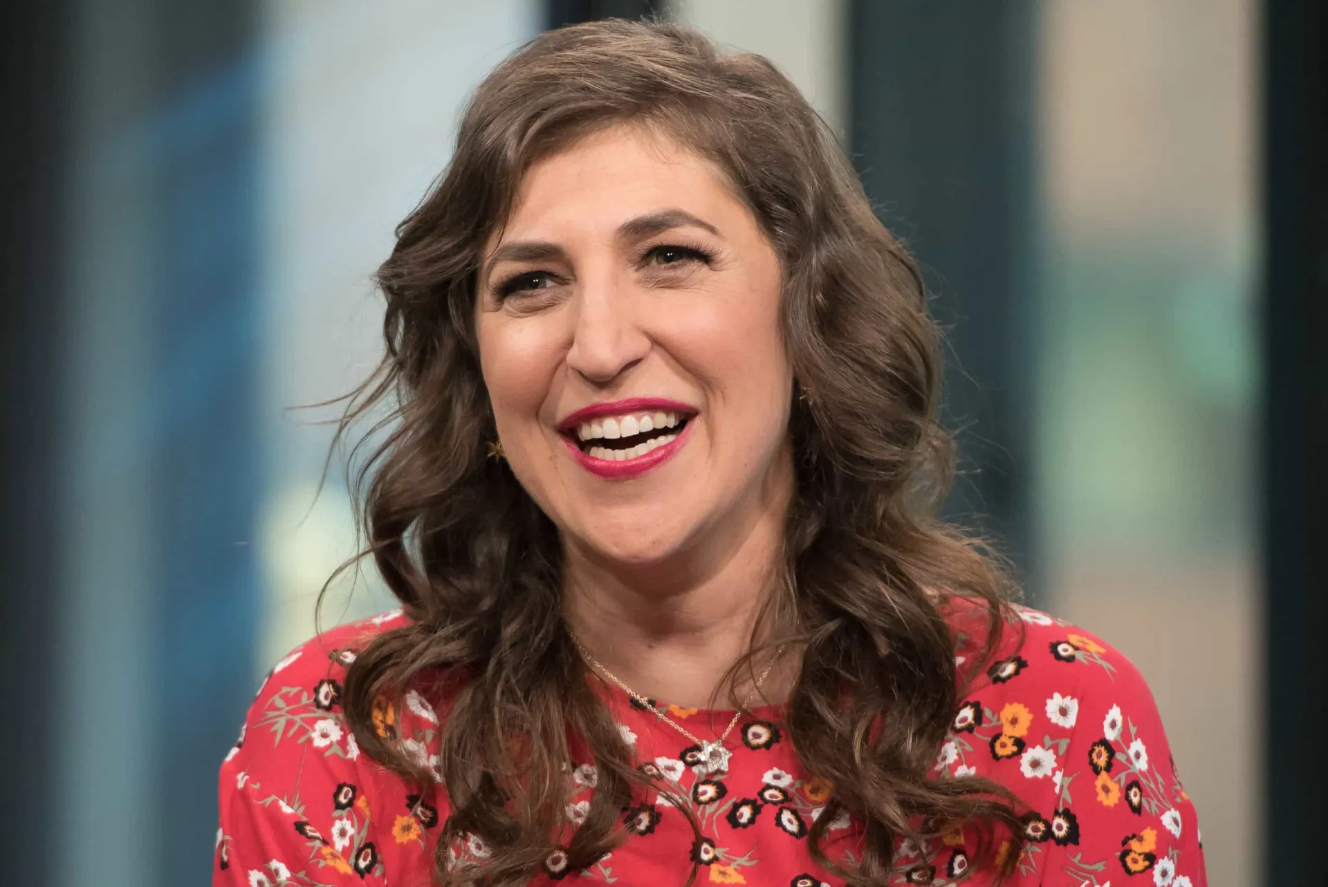 Mayim Bialik como a personagem Amy Farrah Fowler em 'The Big Bang Theory', com um sorriso tímido.