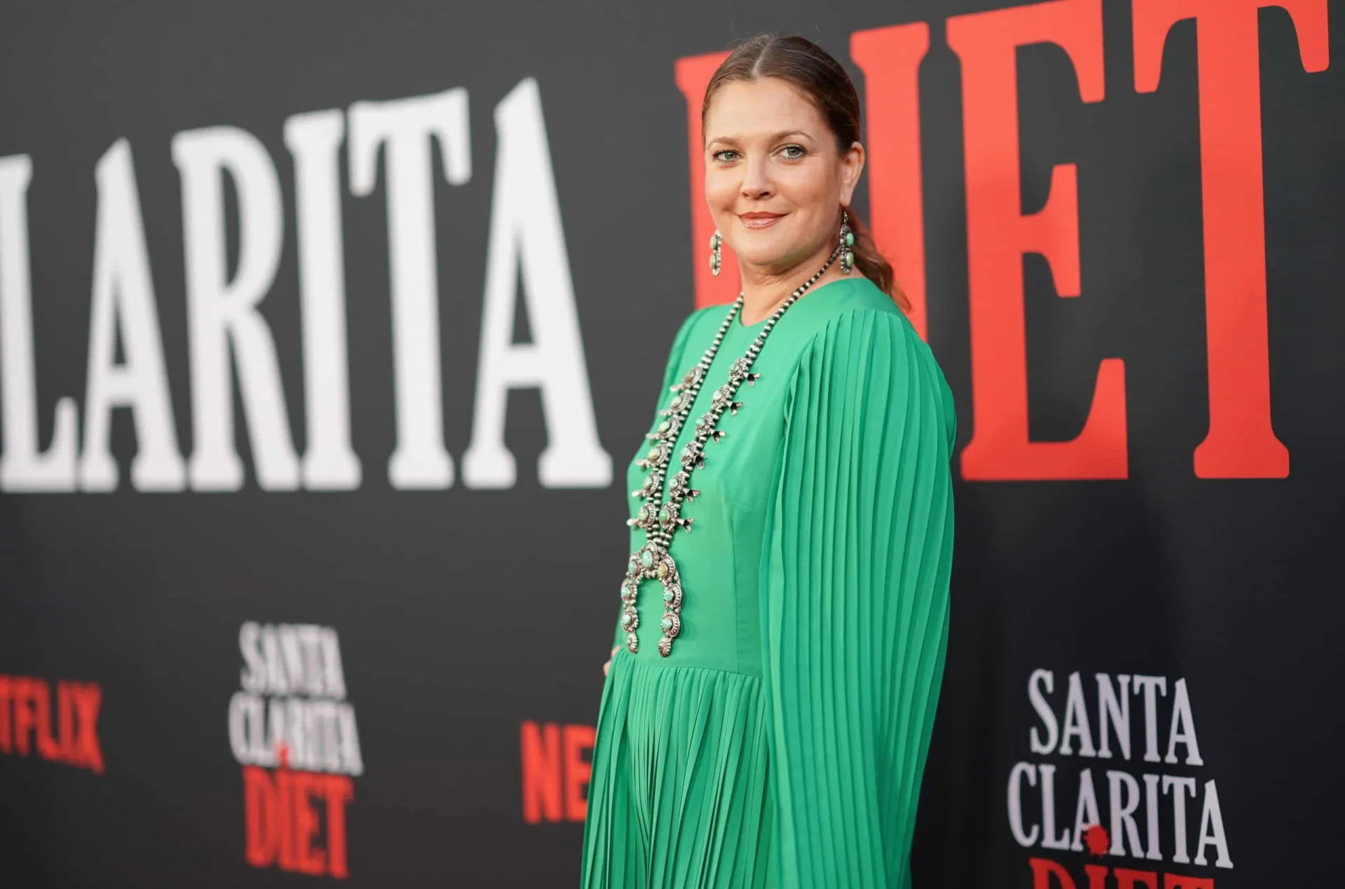 Drew Barrymore adulta, com um sorriso largo e contagiante, agora uma apresentadora de sucesso.