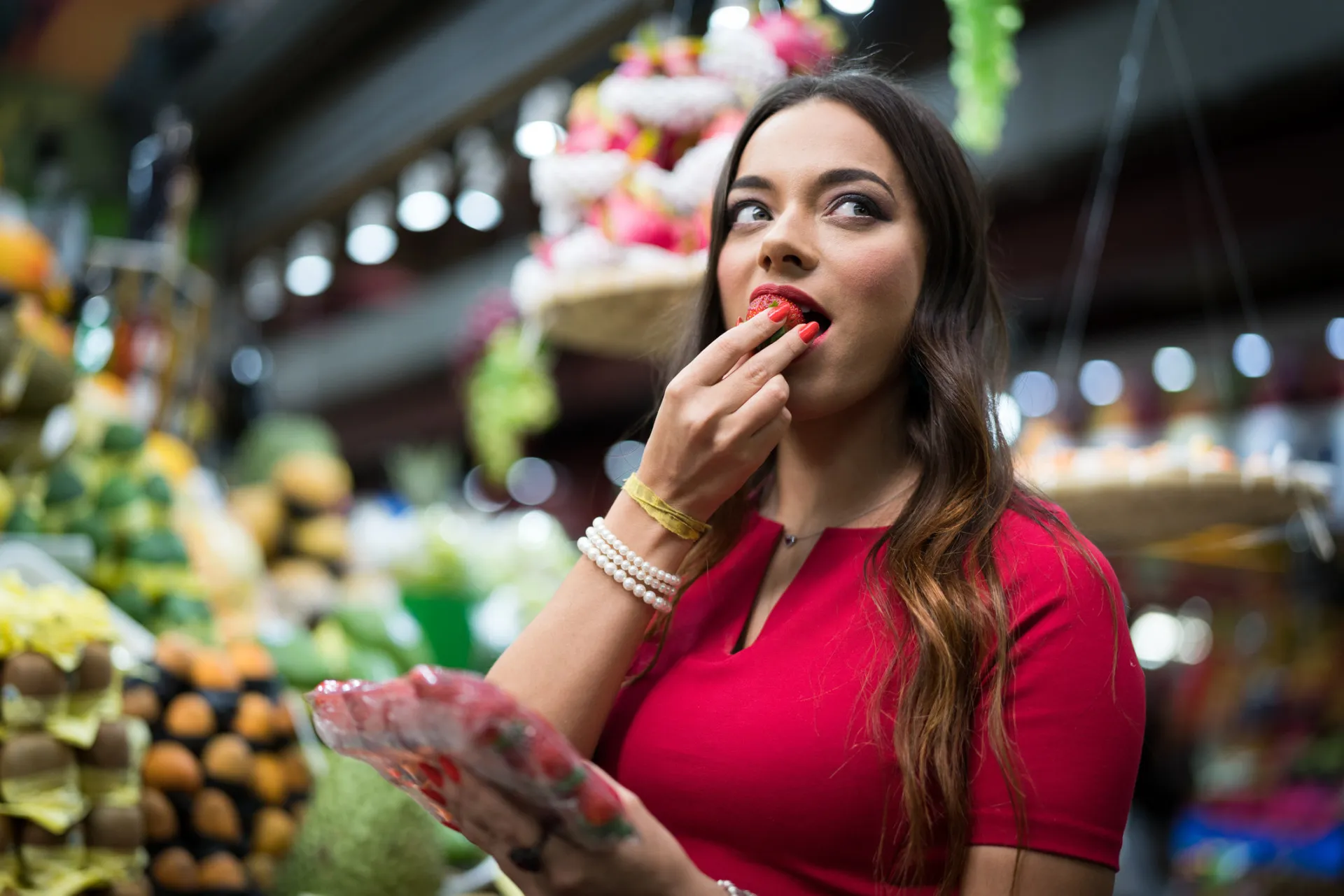 Uma pessoa comendo uma uva diretamente do cacho dentro de um supermercado, antes de pagar.