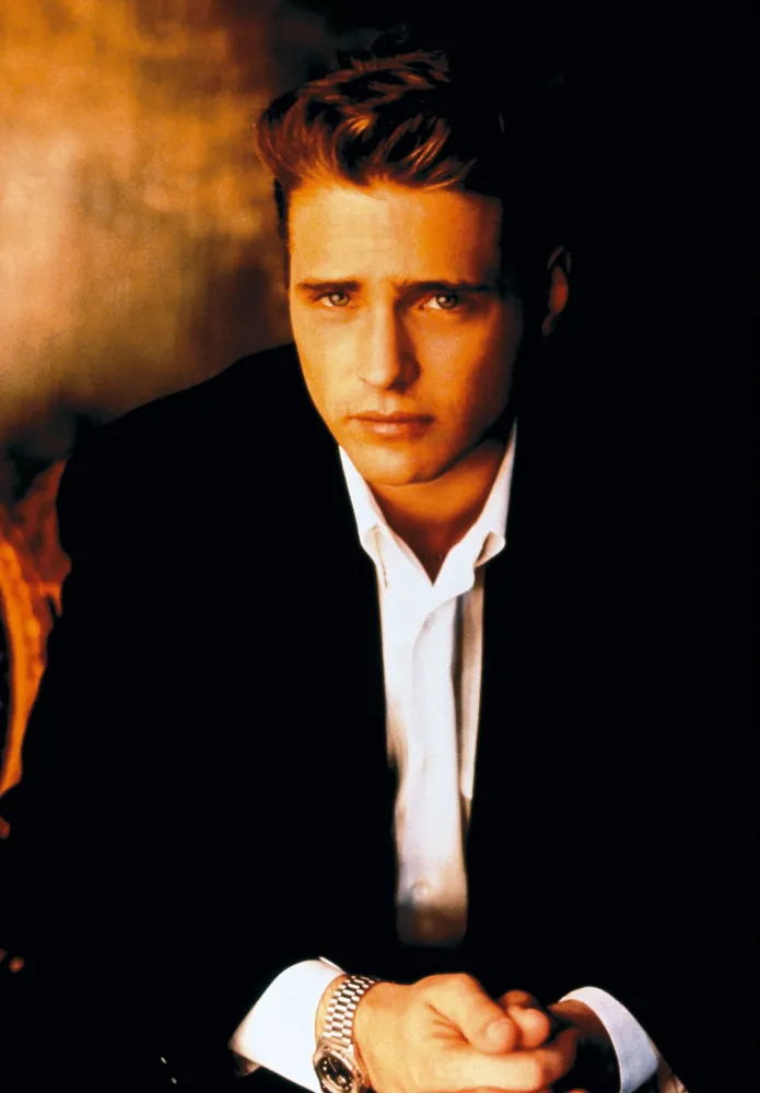 Jason Priestley em um evento de gala, elegante e sorrindo para as câmeras.