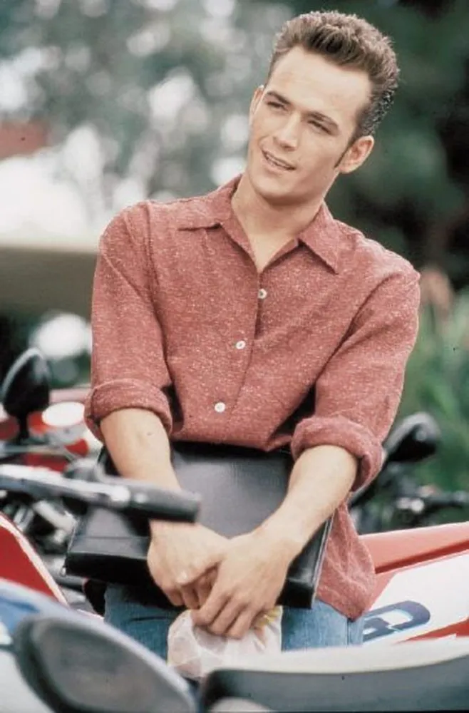 Luke Perry como o charmoso e rebelde Dylan McKay, com seu topete icônico.
