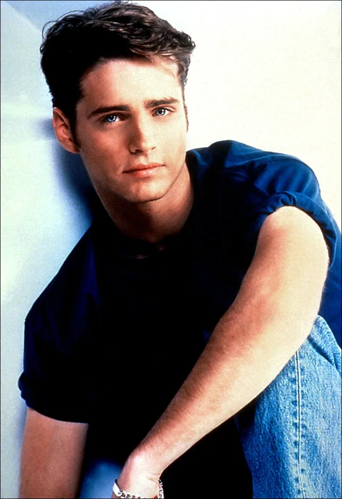 Jason Priestley como Brandon Walsh, com um olhar sério e cabelo característico dos anos 90.