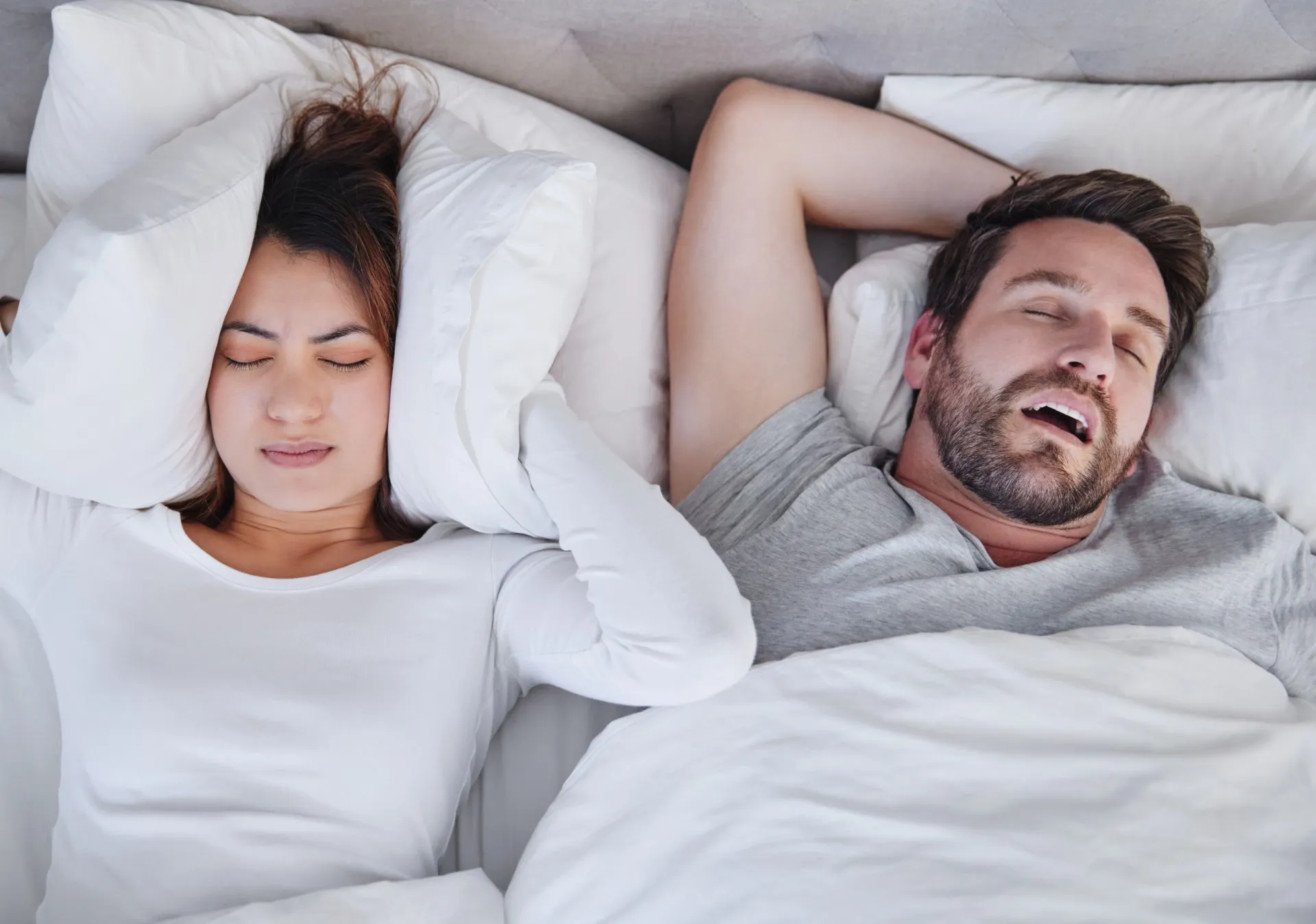Homem roncando alto na cama, com a parceira visivelmente incomodada.