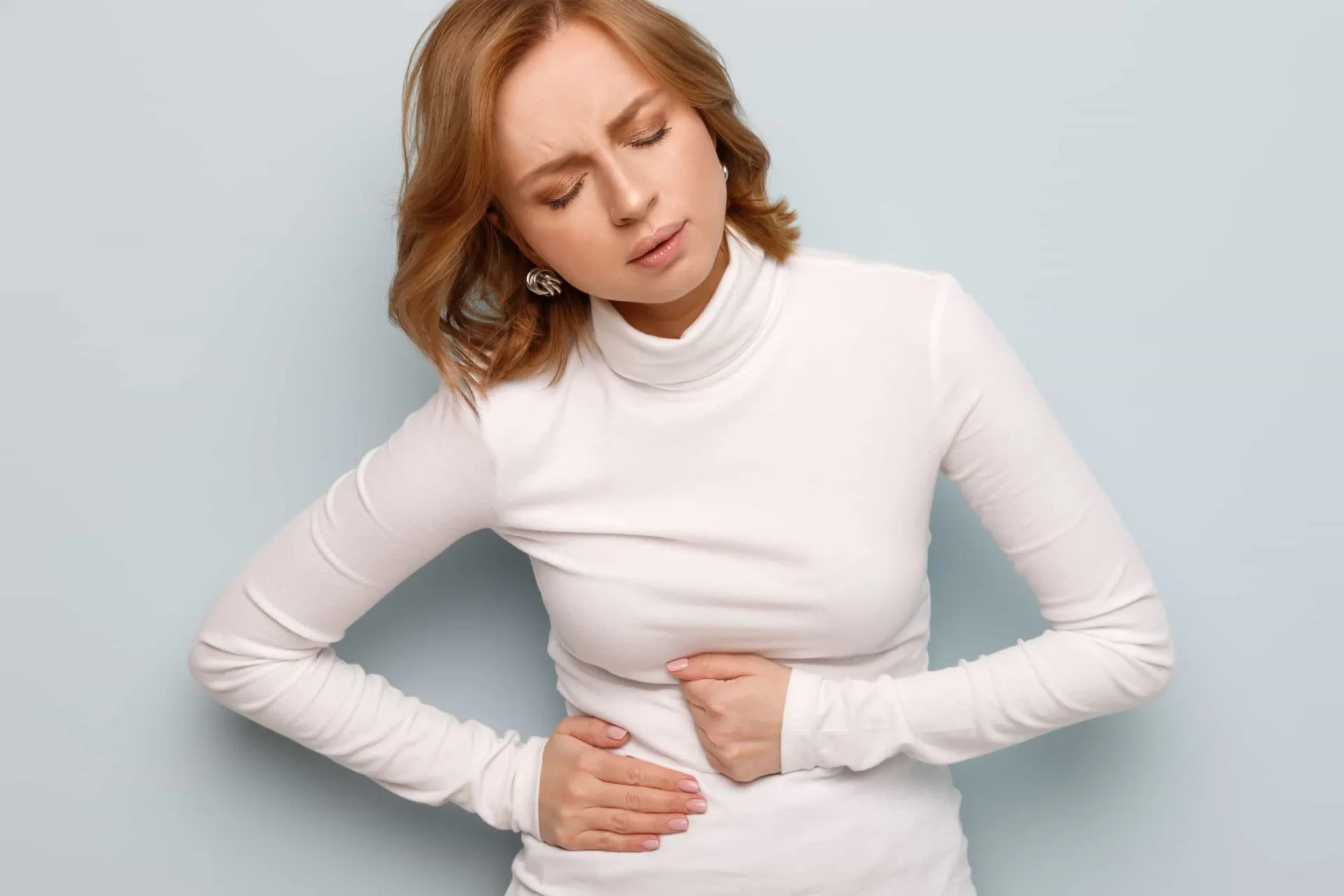Pessoa deitada no chão em posição fetal, tentando aliviar a dor abdominal.