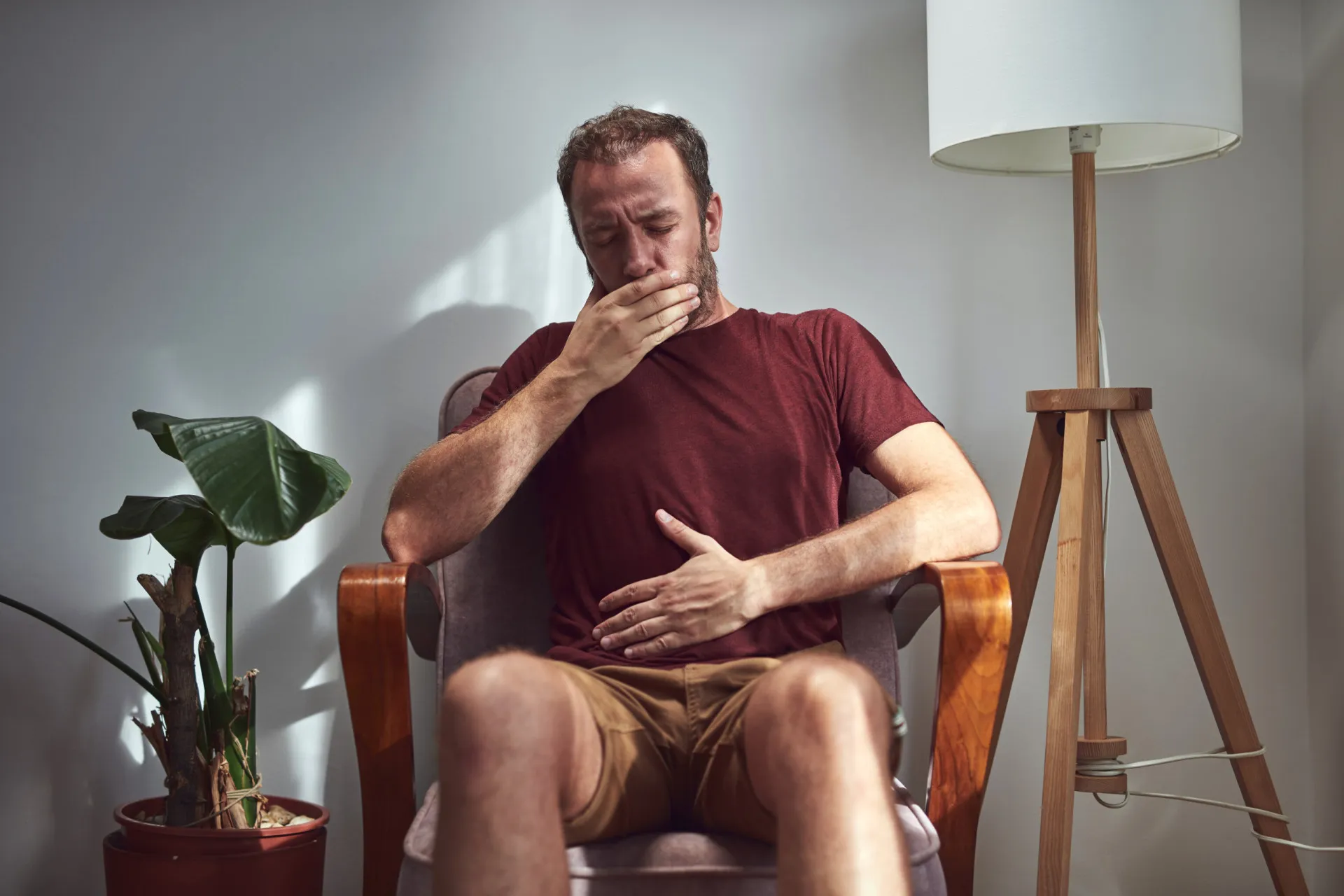 Pessoa sentada em um sofá, visivelmente desconfortável com inchaço abdominal e ruídos na garganta.