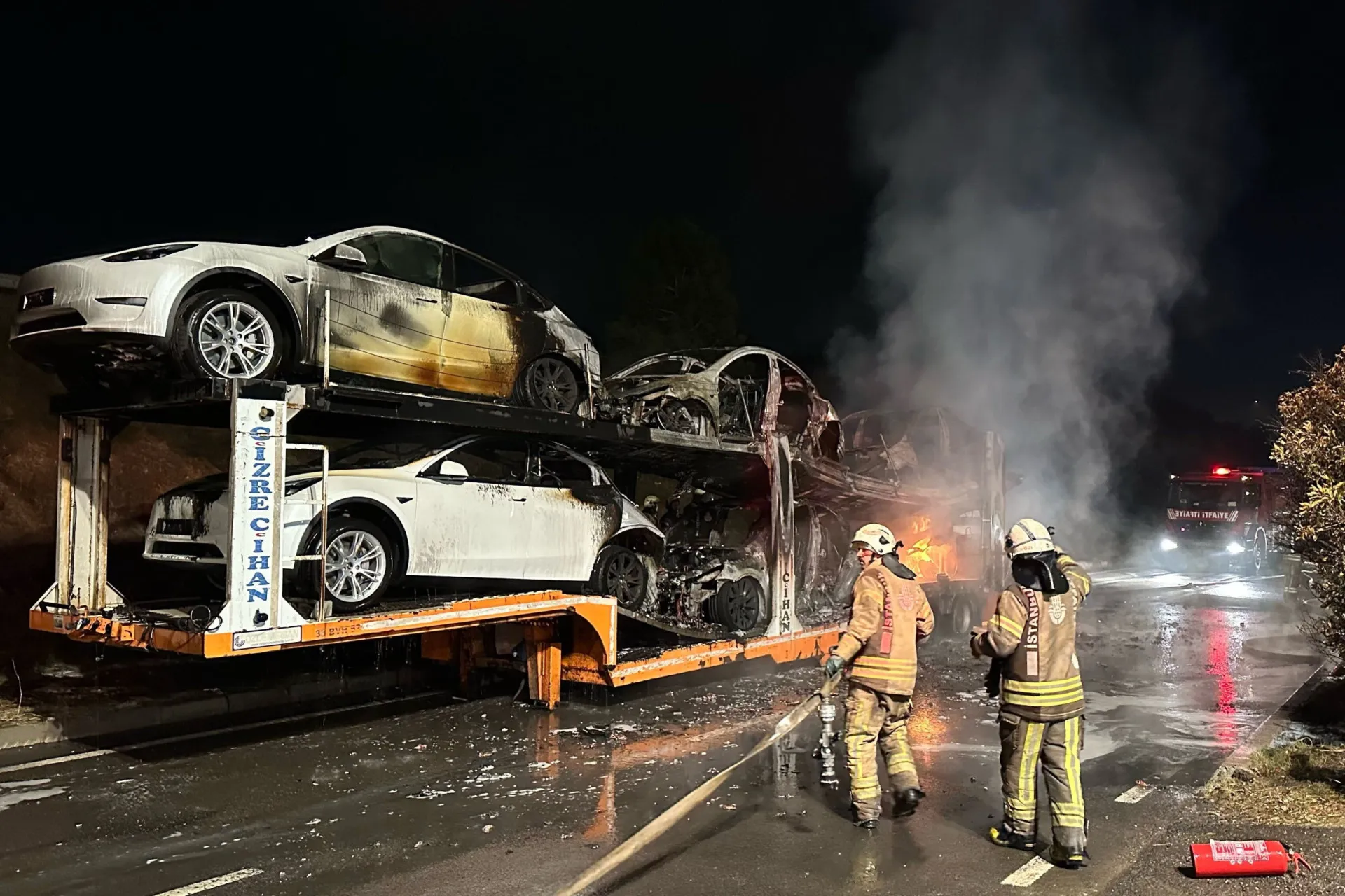 Bombeiro inspecionando um carro elétrico queimado dias após o incêndio inicial.
