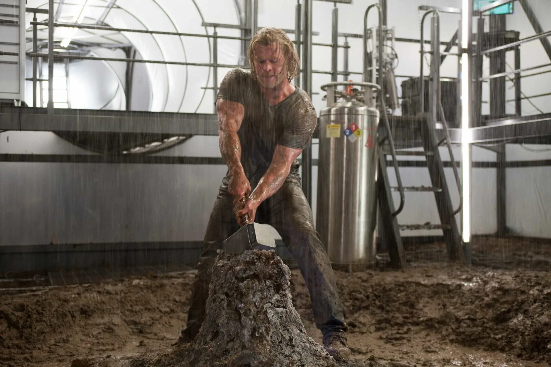 Chris Hemsworth com o cabelo comprido de Thor e um físico extremamente musculoso, segurando o martelo Mjolnir.