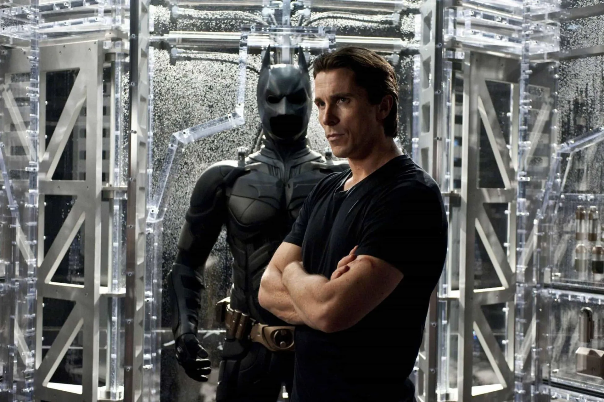 Christian Bale como Batman, com o capuz e um físico musculoso que preenche a armadura do herói.