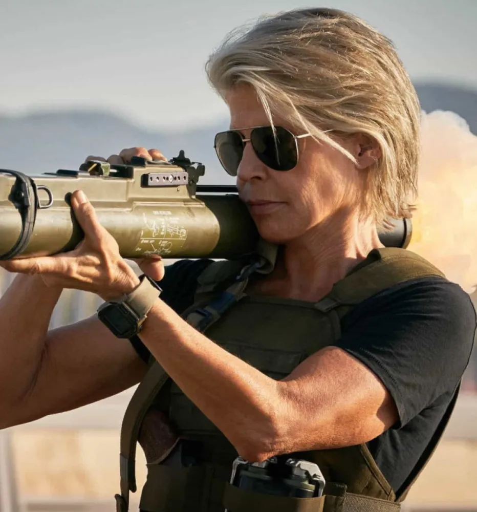 Linda Hamilton como Sarah Connor em 'Exterminador do Futuro: Destino Sombrio', com braços musculosos e um olhar endurecido.