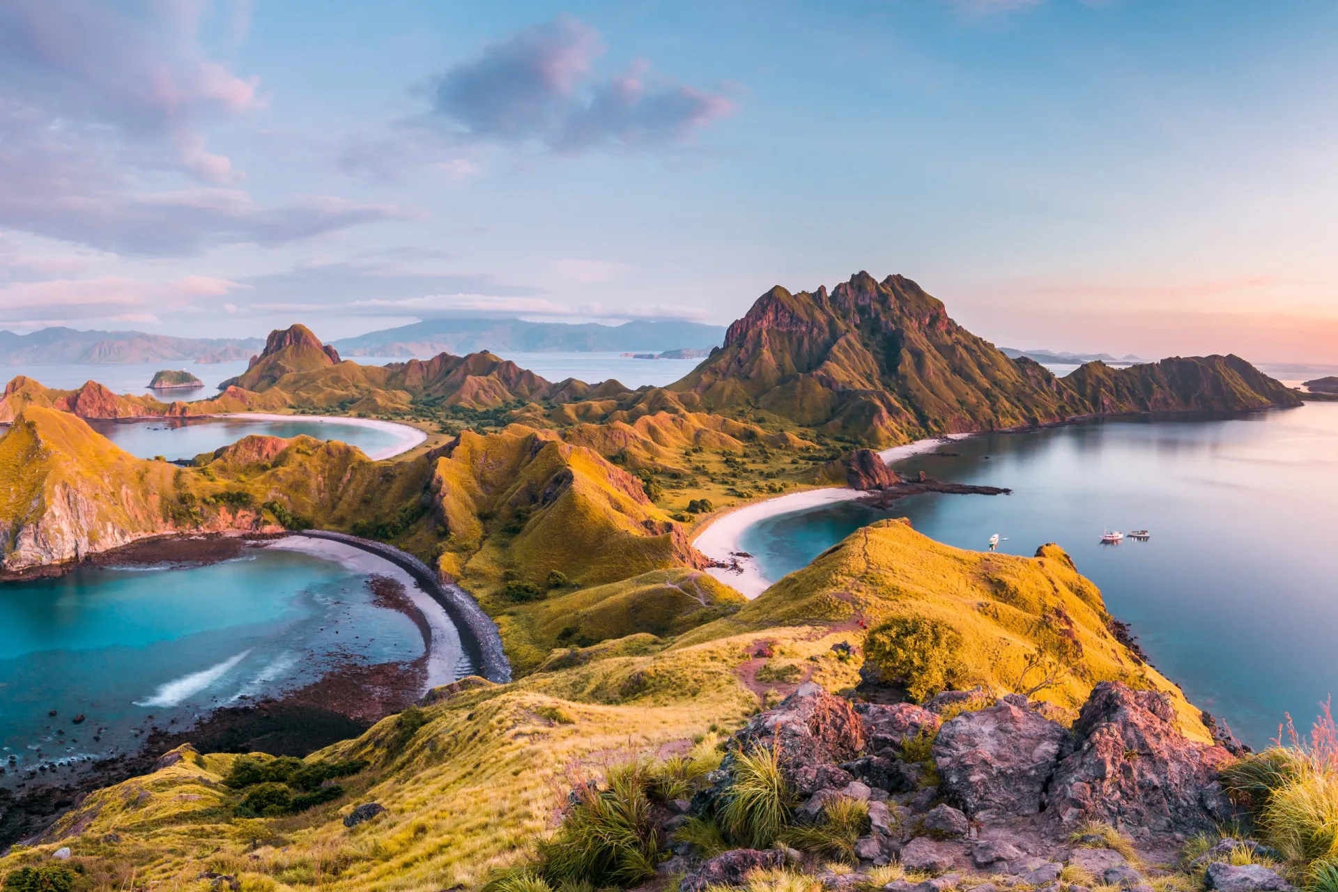 Praia de areia rosa na Ilha de Komodo, com colinas áridas ao fundo.