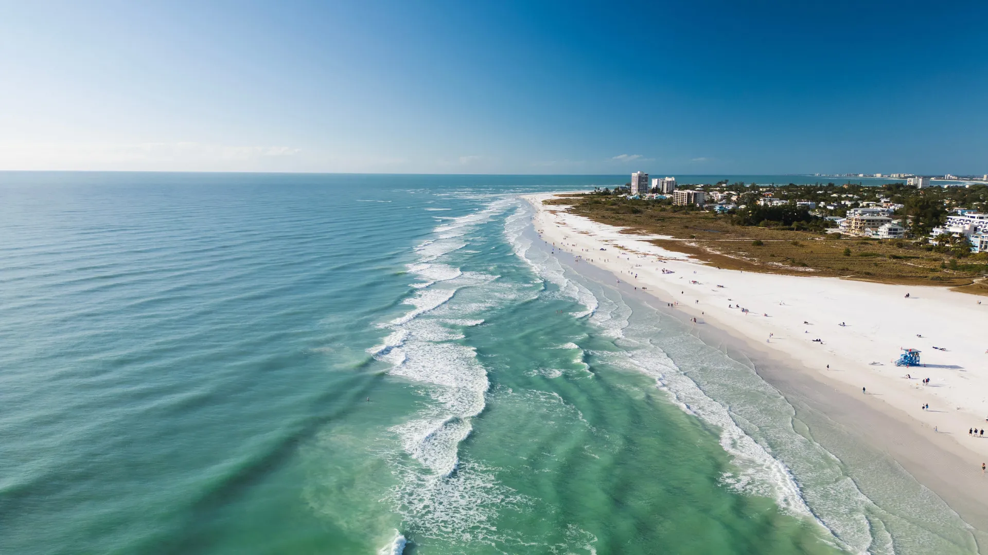 Areia branca e fina de Siesta Beach na Flórida, com cadeiras de praia coloridas.