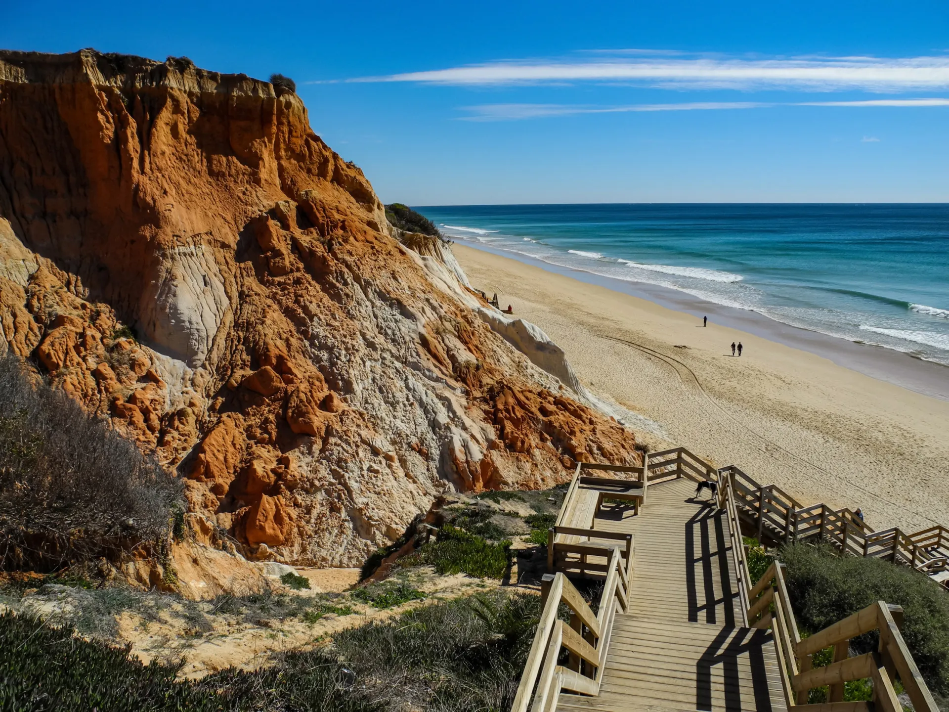 Imponentes falésias avermelhadas contrastando com a areia dourada na Praia da Falésia, em Portugal.