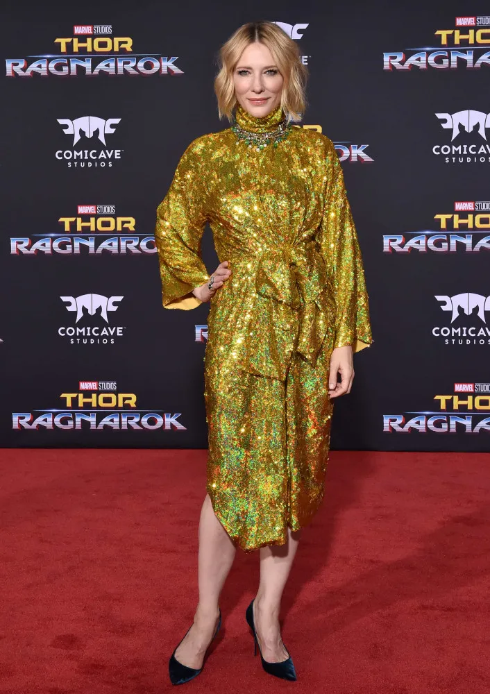 Uma mulher usando joias de ouro e roupas douradas, com uma expressão de realeza e poder.
