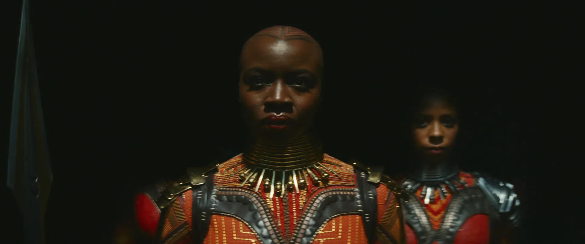 Okoye, a general das Dora Milaje, com sua cabeça raspada e lança de Vibranium em punho.