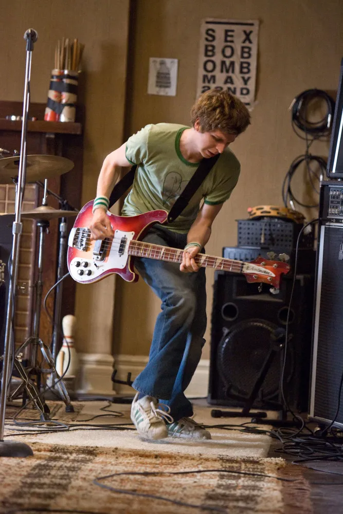 Scott Pilgrim, com sua jaqueta e olhar confuso, em um cenário que lembra um videogame.