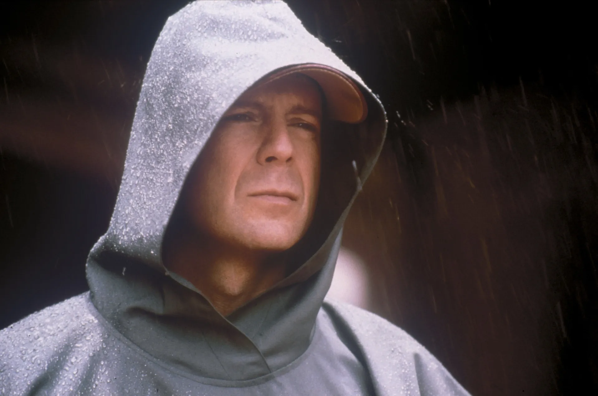 David Dunn, interpretado por Bruce Willis, com sua capa de chuva verde, parecendo um herói urbano e sombrio.